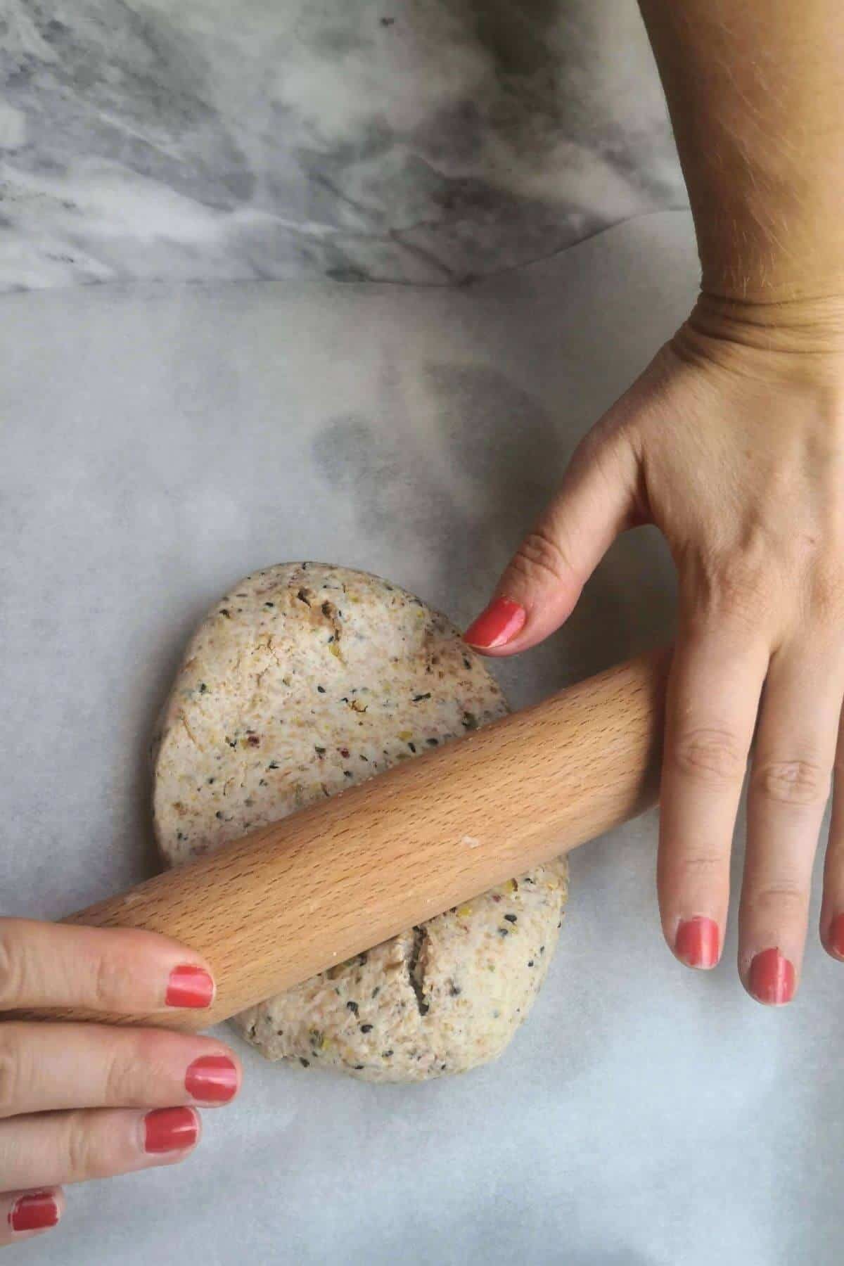Hands rolling out the sourdough discard dough with a wooden rolling pin on baking paper.