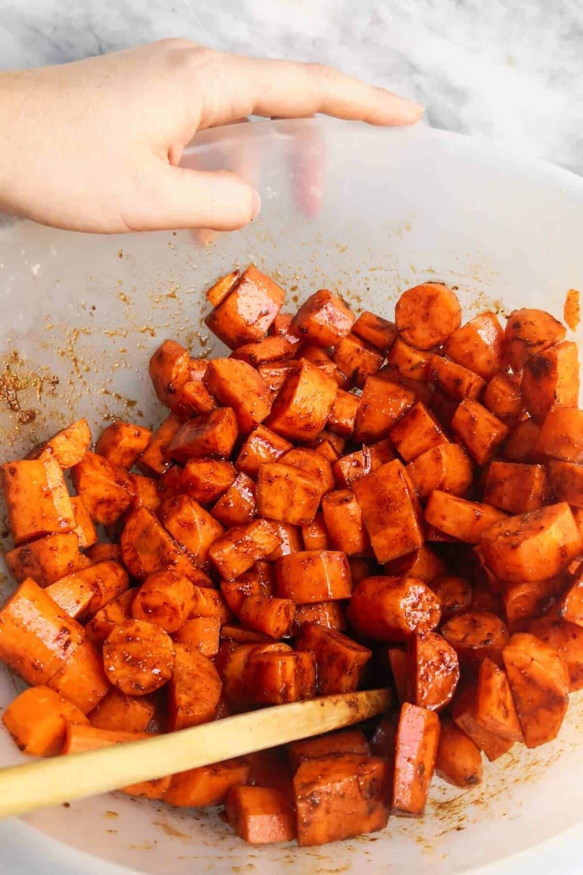 Chopped carrots in a large clear bowl with a wooden spoon inside.