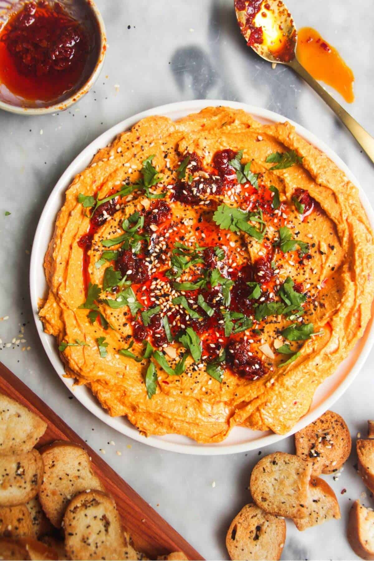 Spicy harissa feta dip on a small white plate, with bagel chips and more harissa on the side.