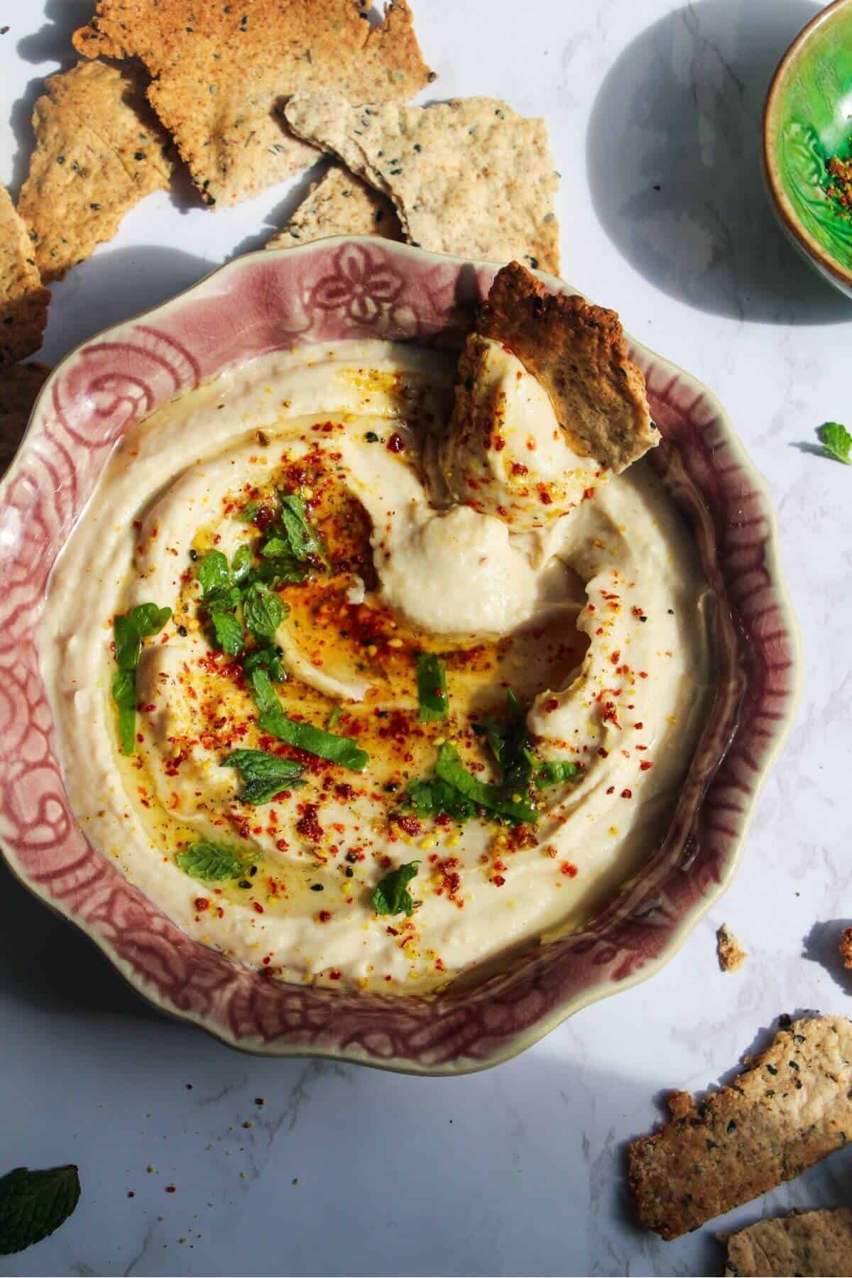 Cracker swirled through white bean dip in a small pink bowl with more crackers on the side.
