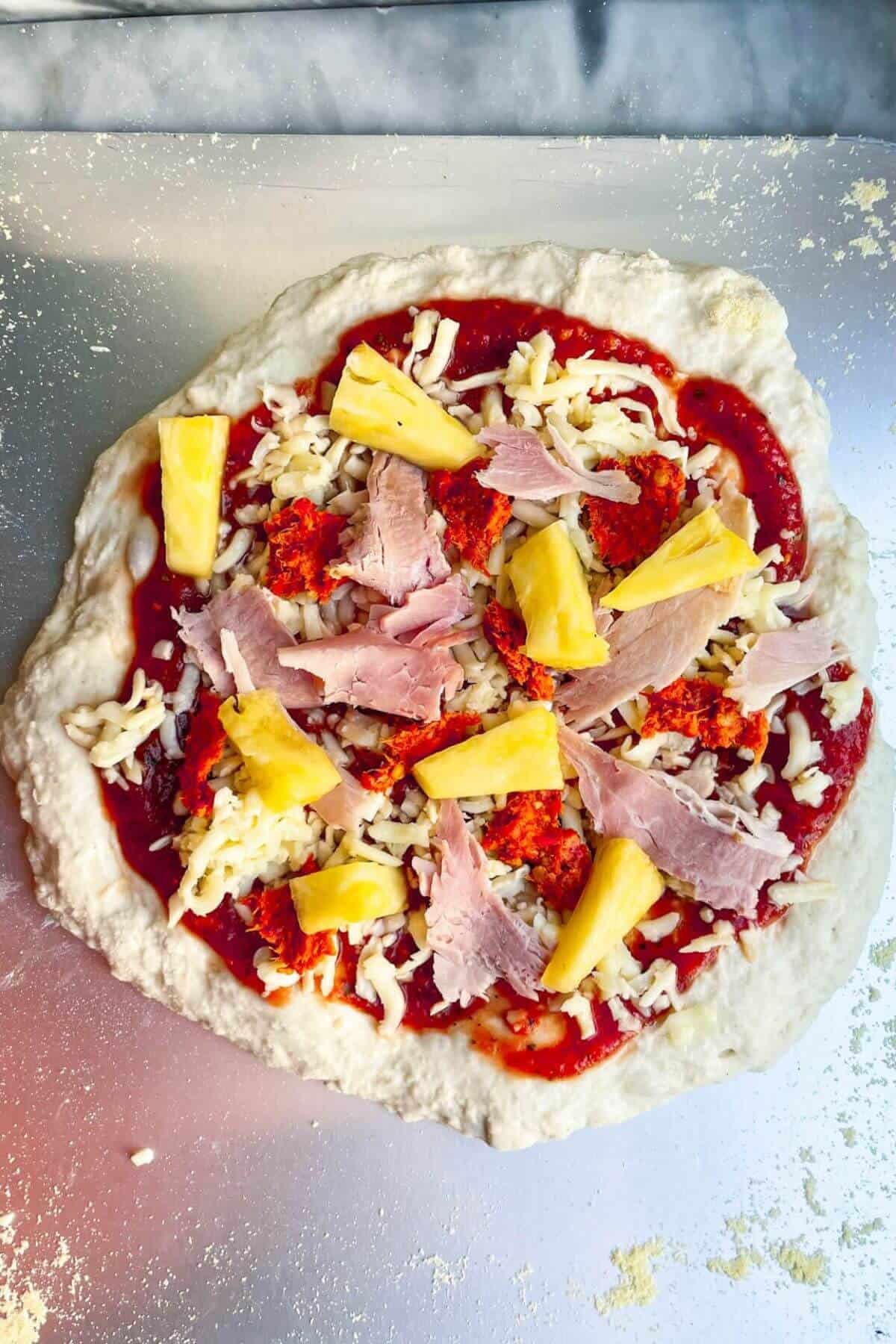 Spicy Hawaiian pizza on steel pizza peel ready to be cooked.