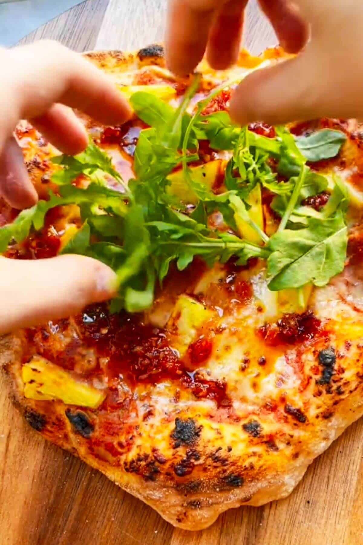 Adding a pile of rocket on top of spicy Hawaiian pizza.