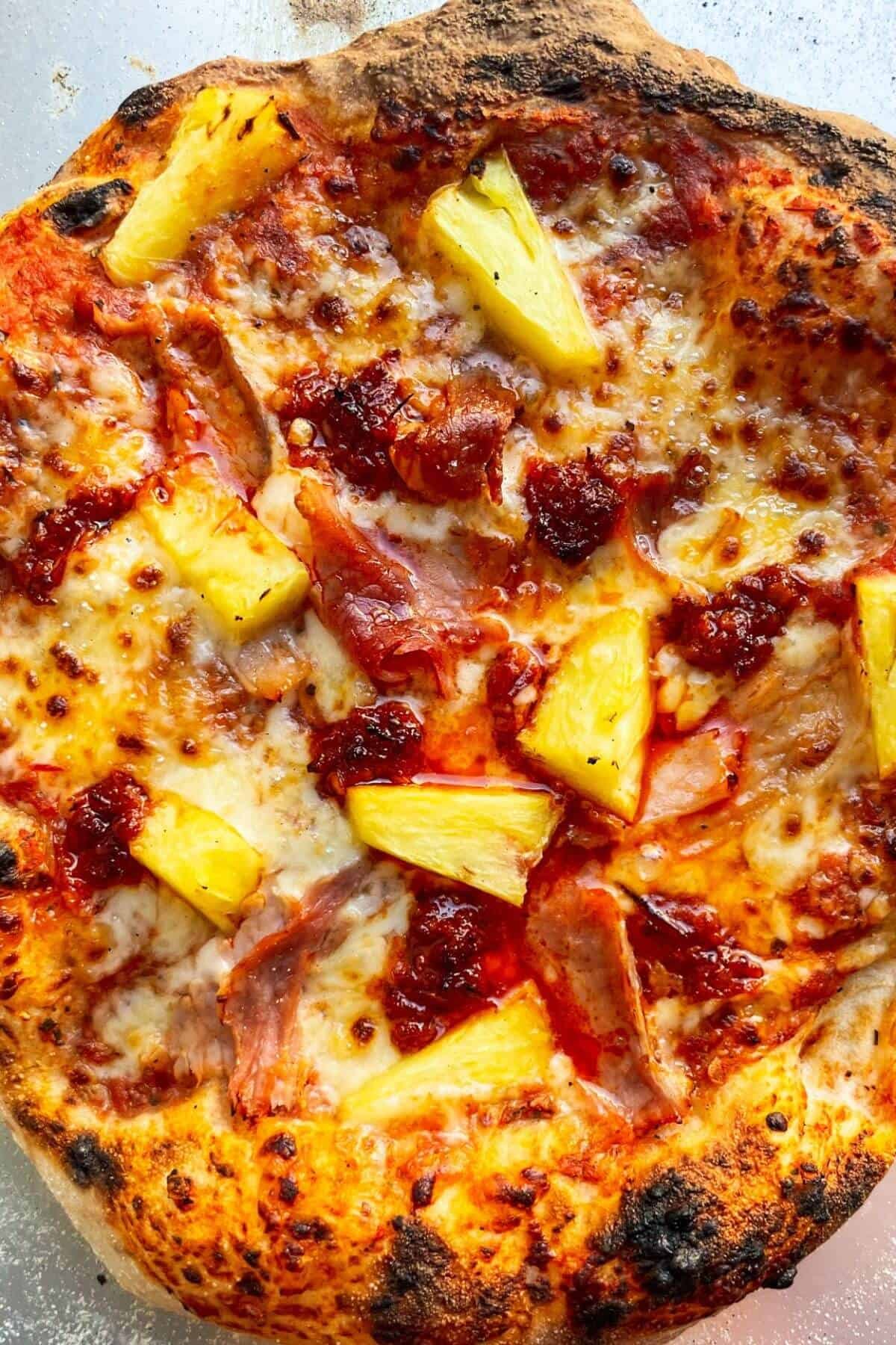 Close up of spicy Hawaiian pizza on silver pizza peel.