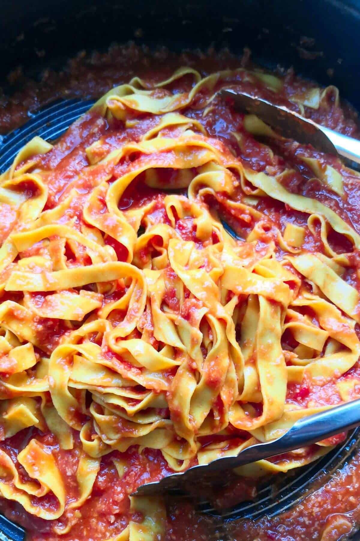 Nduja pasta being tossed through sauce with large silver tongs in a pan.