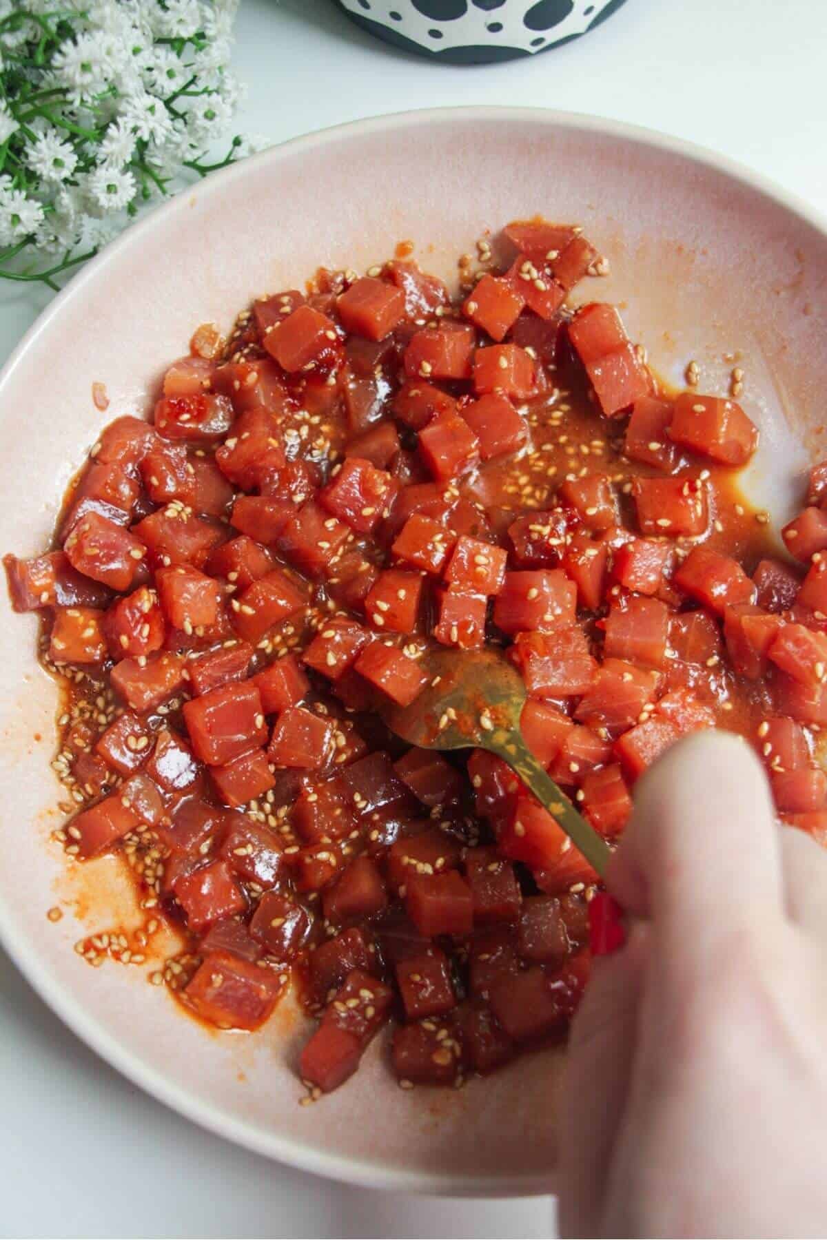 Mixing diced tuna through marinade in a bowl.