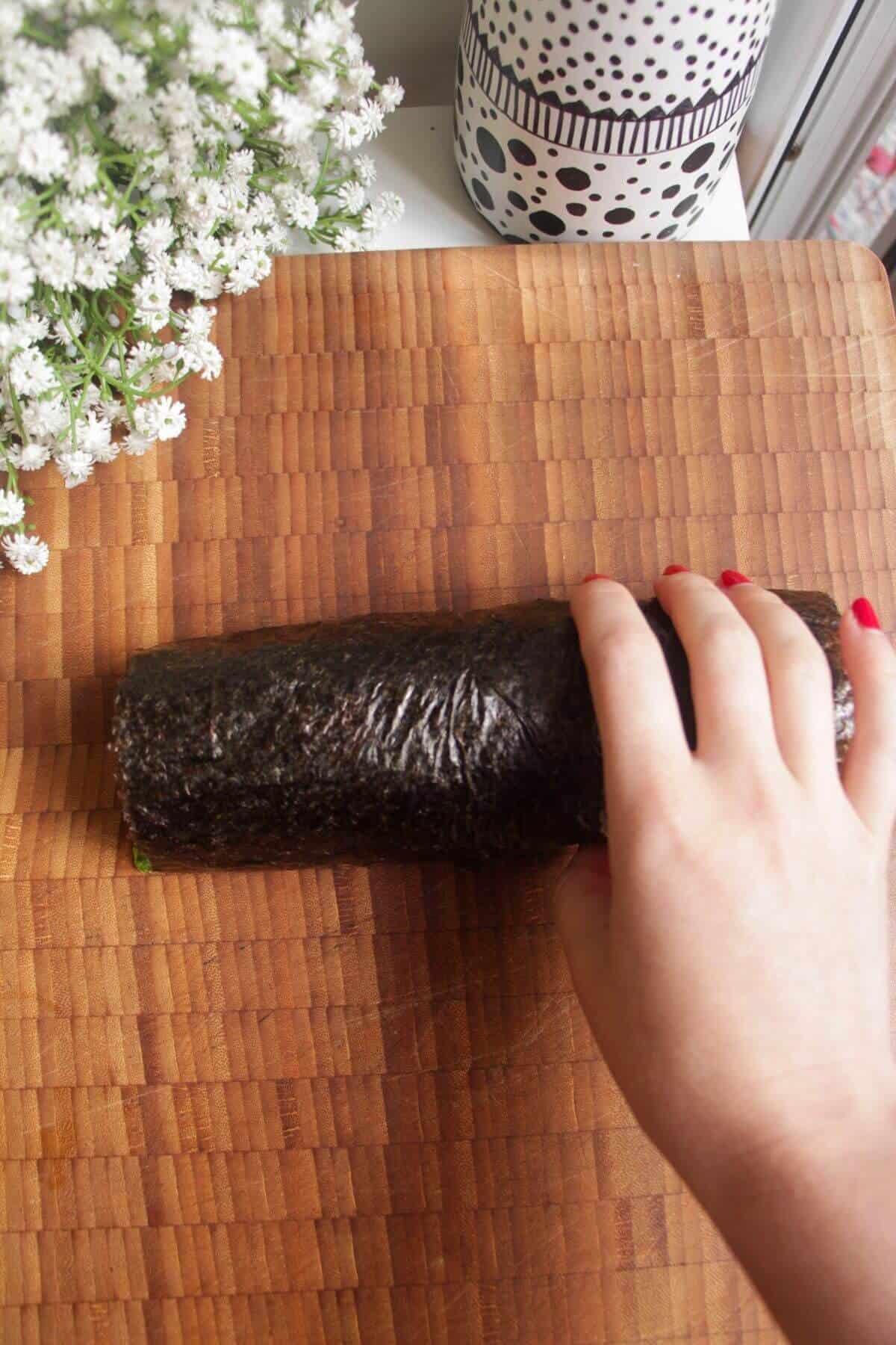 Hand rolling up sushi burrito on a wooden board.