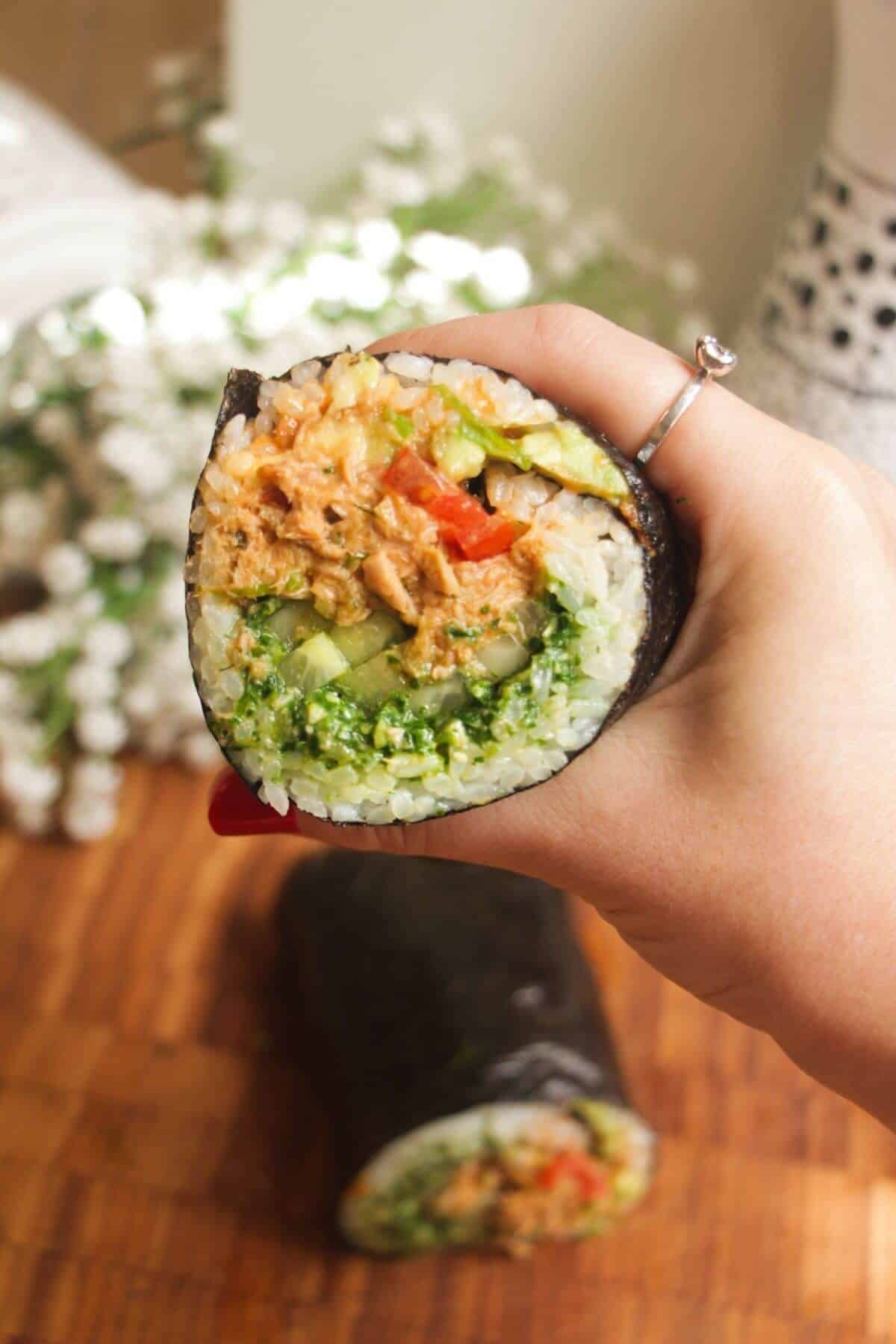Hand holding sliced sushi burrito.