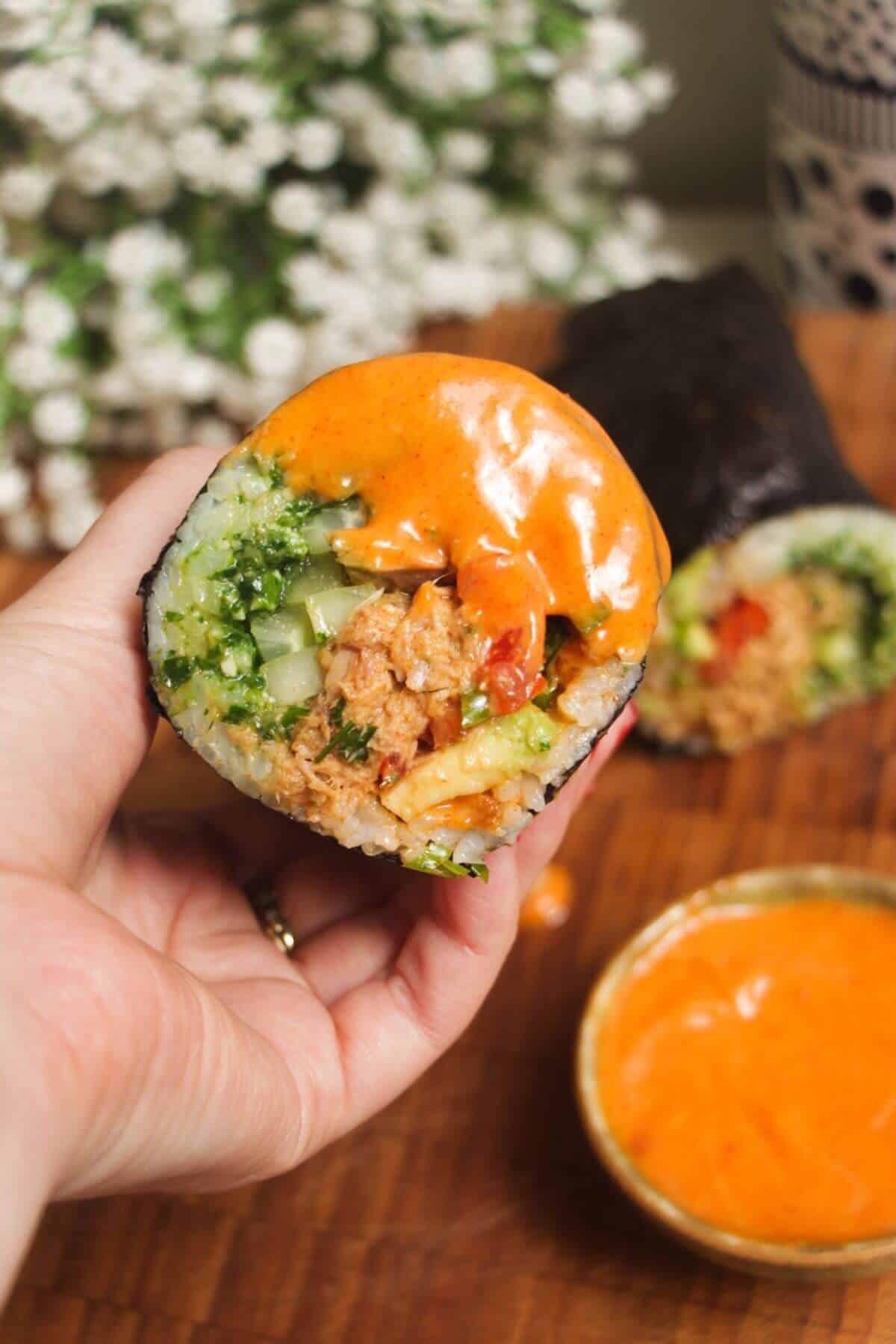 Hand holding sliced sushi burrito with spicy aioli on the side.