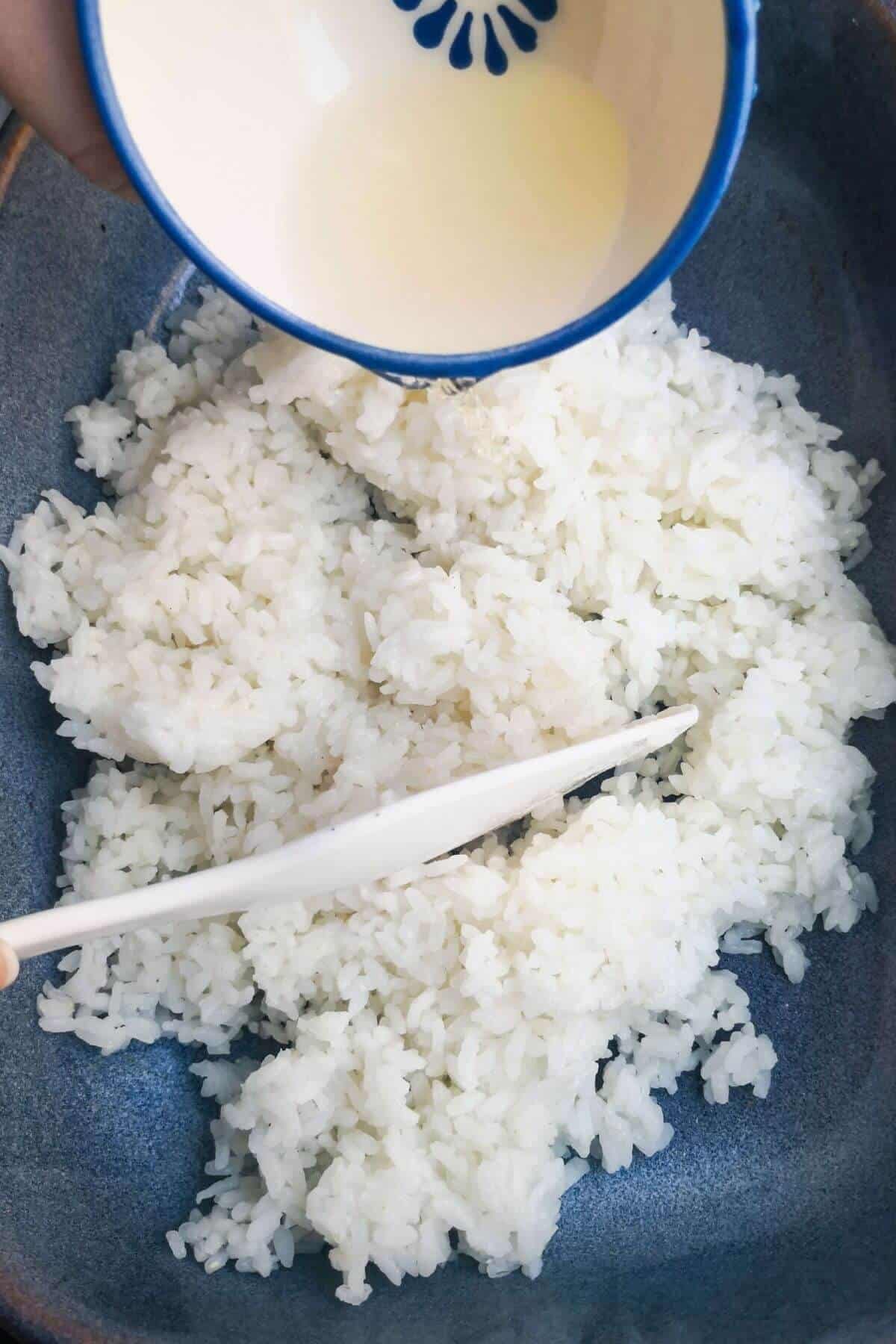 Rice vinegar being poured into sushi rice in a small blue dish.