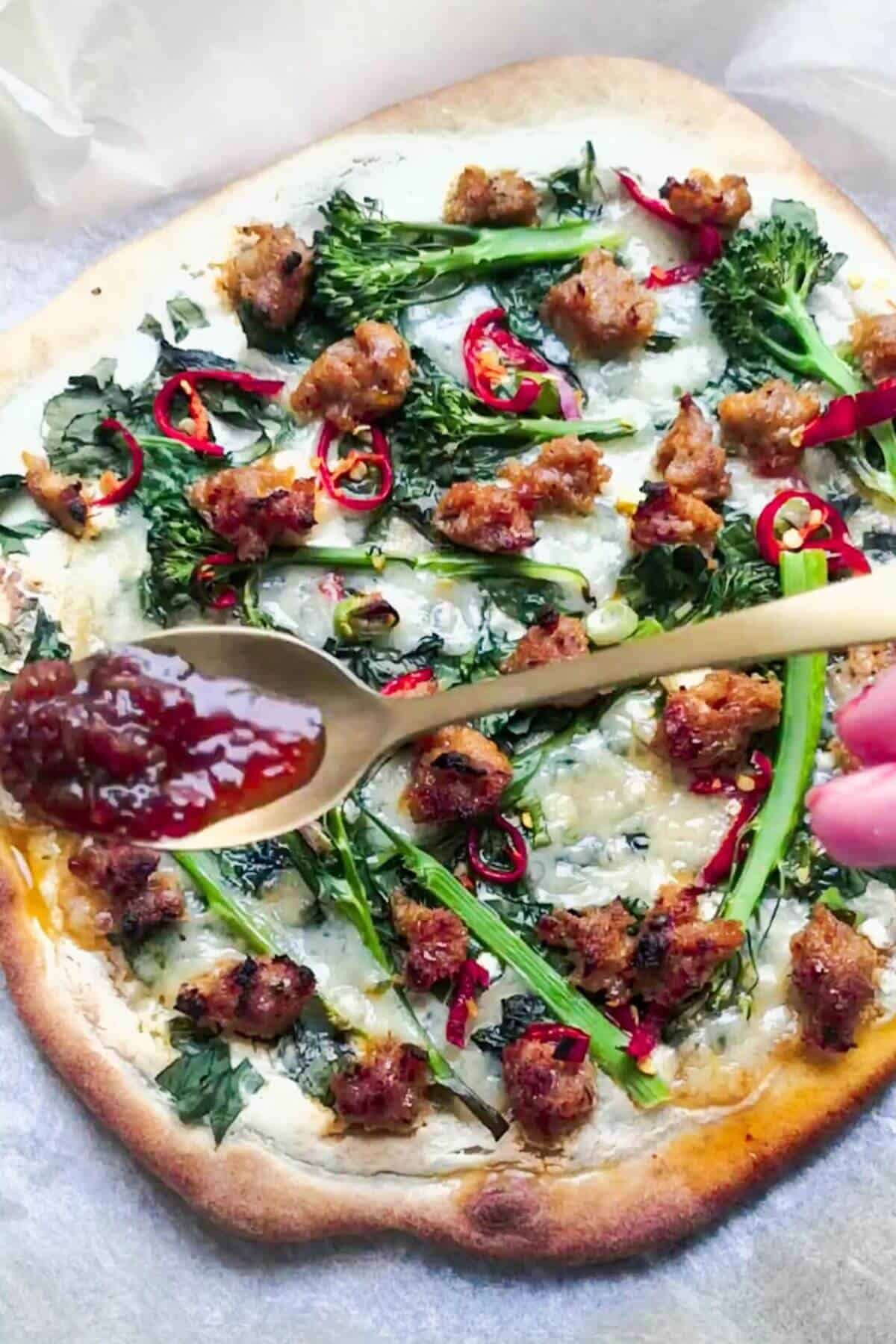 Chilli jam being drizzled on top of sausage ricotta pizza.