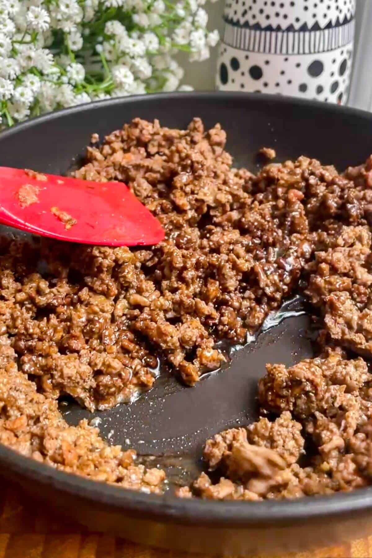 Spatula stirring sticky ground beef in a pan.