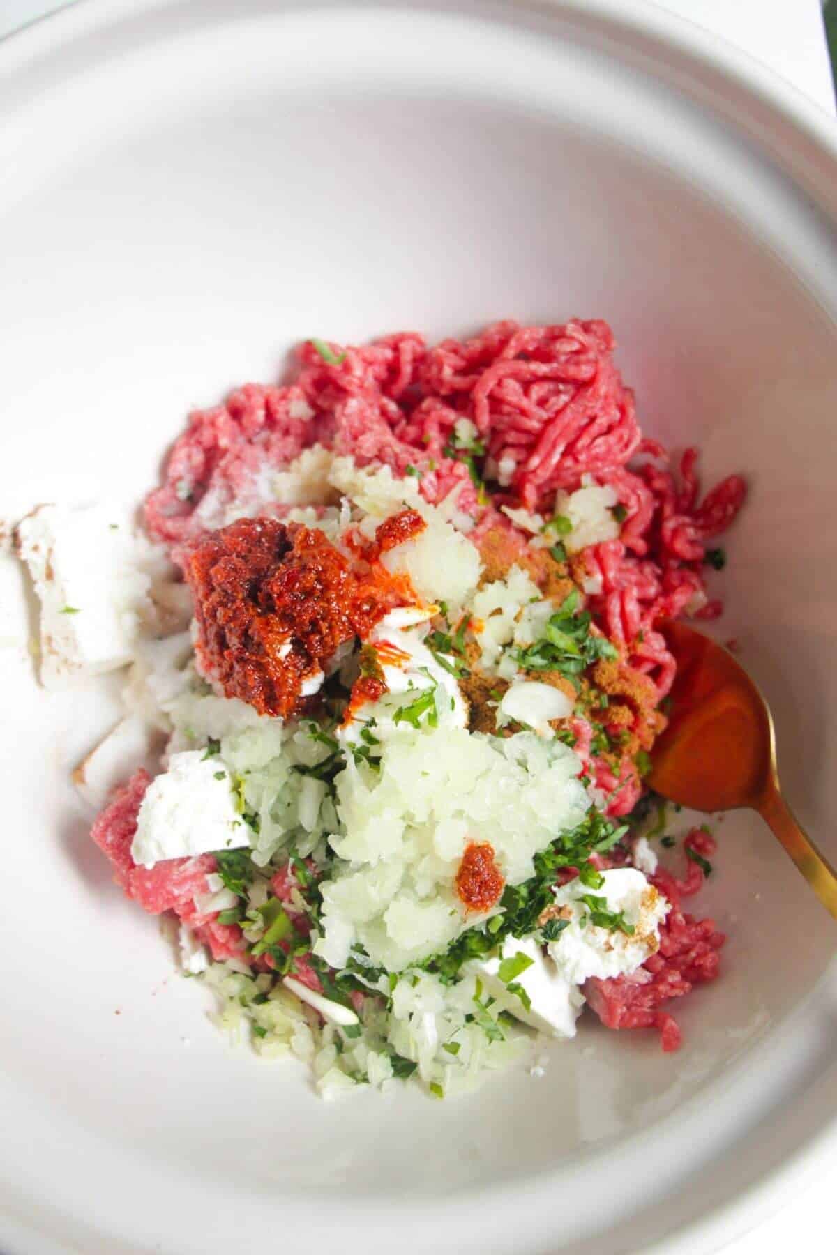 Ground beef, spices, onion, harissa paste and feta in a mixing bowl.