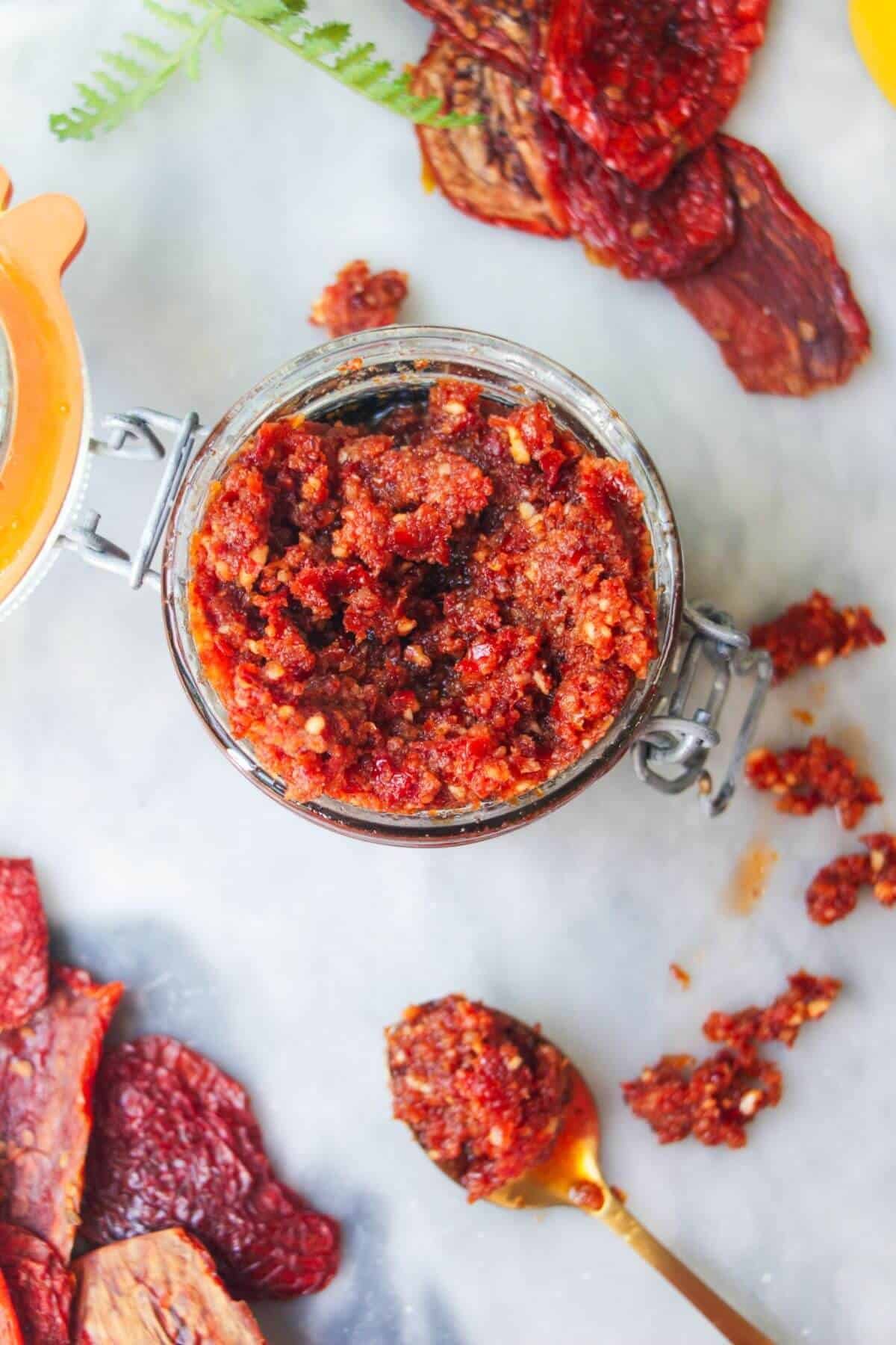 Sun dried tomato pesto in a glass jar with a gold spoon in it.
