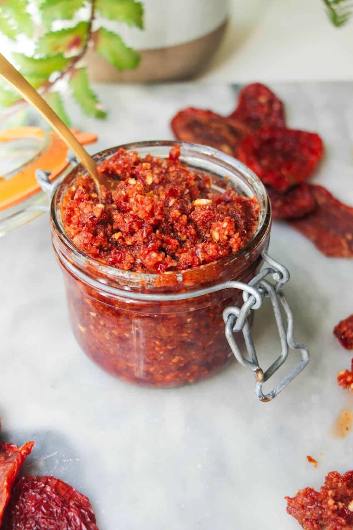 Sun dried tomato pesto in a glass jar with a gold spoon in it.