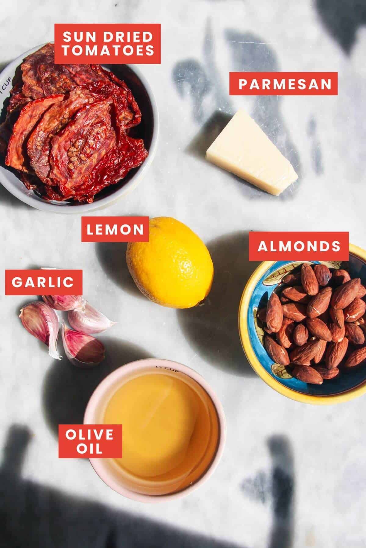 Ingredients for sun dried tomato pesto laid out on a grey marble background and labelled.