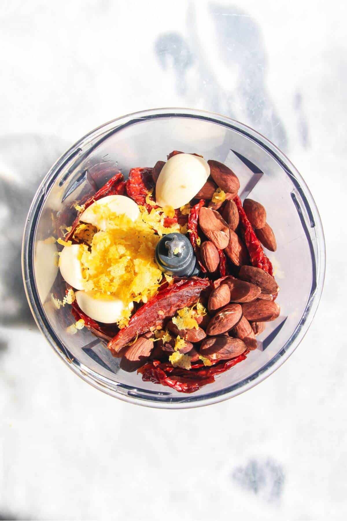 Ingredients for sun dried tomato pesto in a small food chopper.