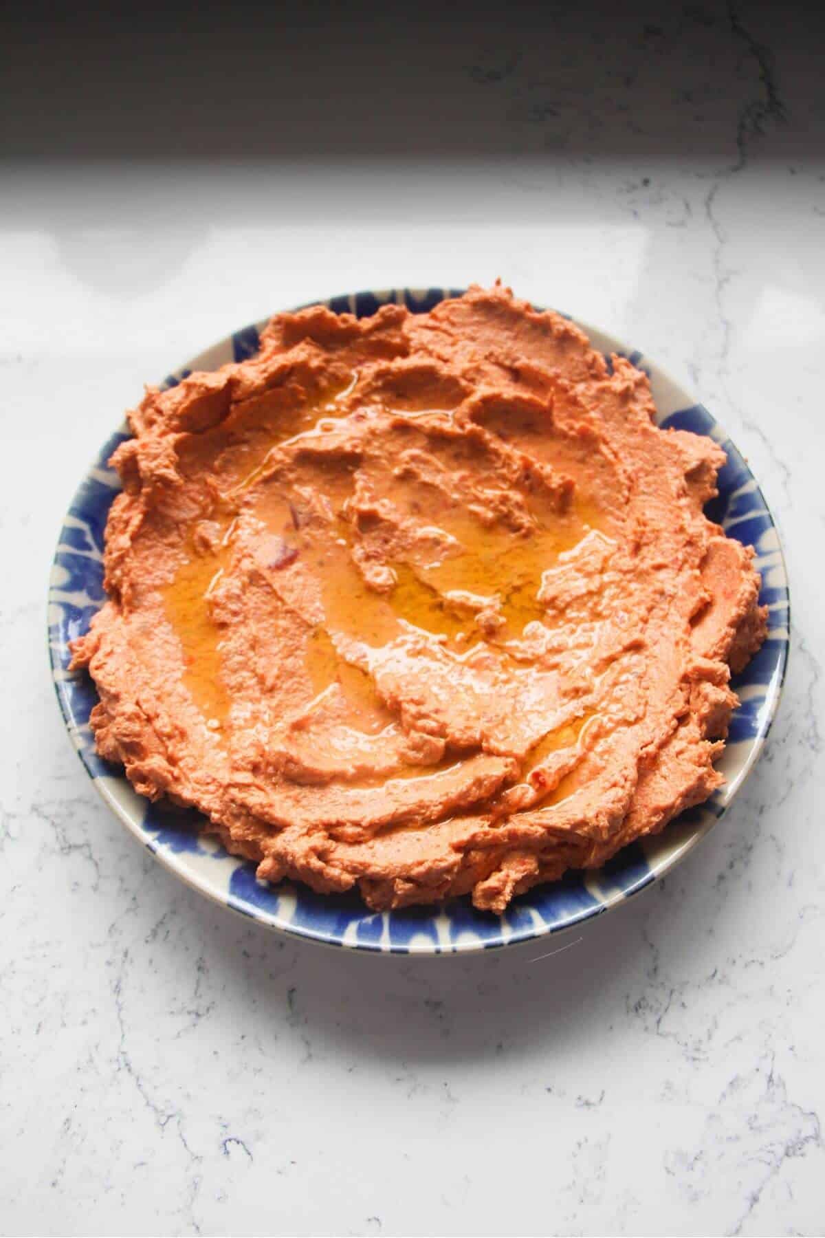 Sundried tomato feta dip smoothed out onto a small plate and drizzled with olive oil.