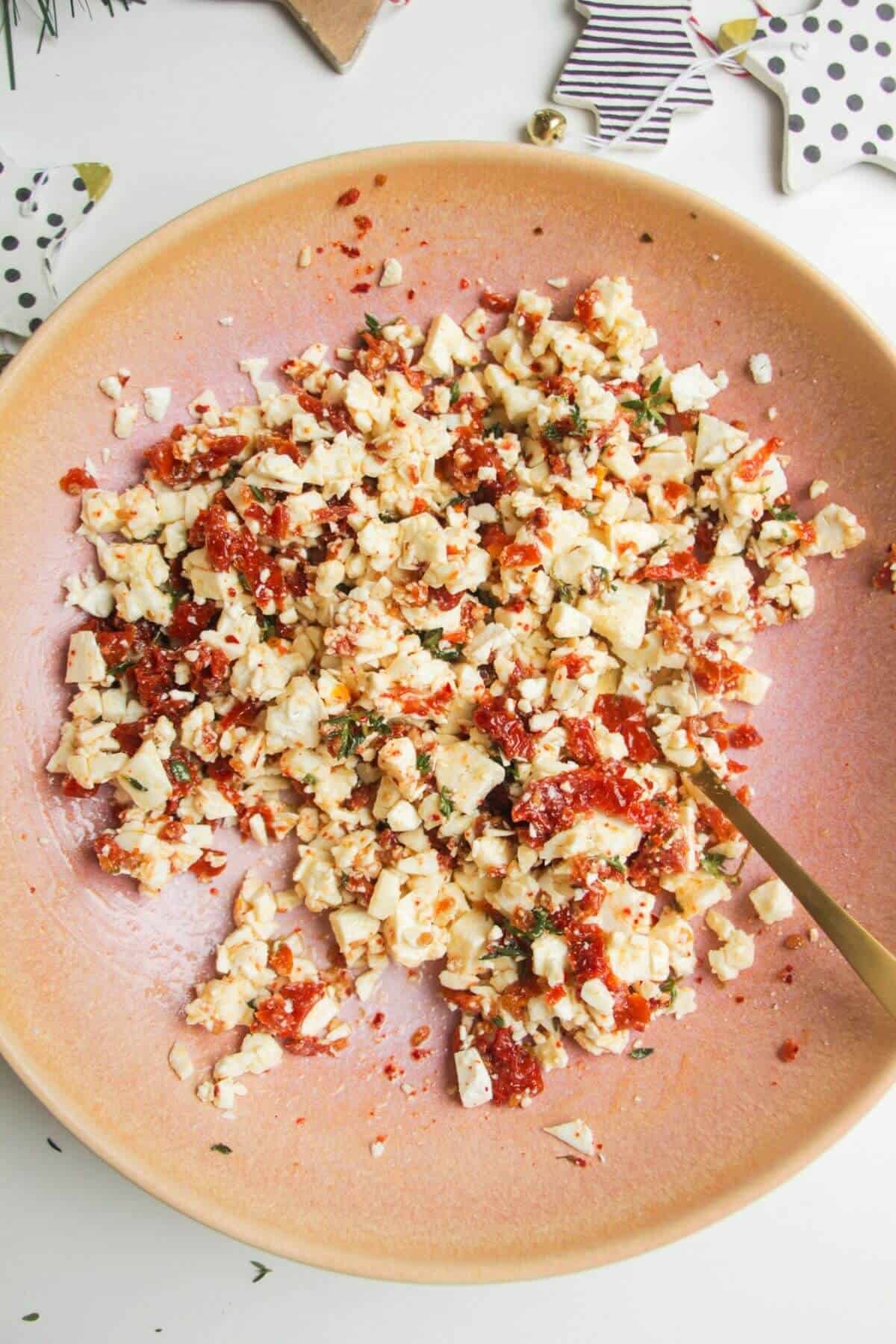 Chopped sundried tomatoes and feta in a pink mixing bowl.