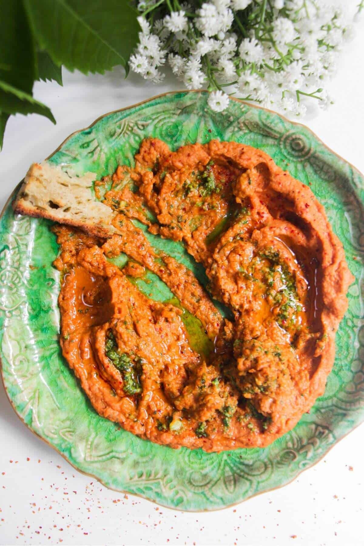 Sundried tomato basil hummus on a green plate with a piece of bread on the side.