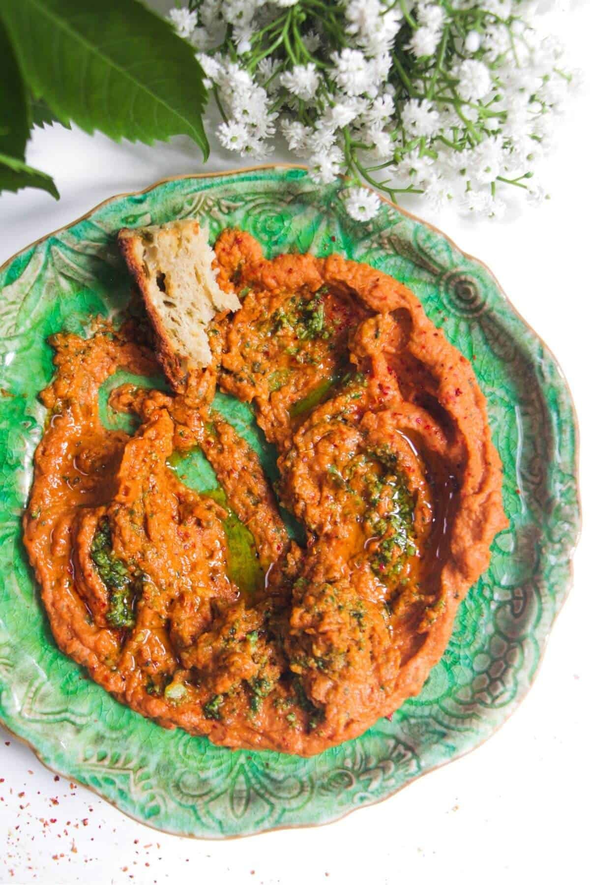 Sundried tomato basil hummus on a green plate with a piece of bread on the side.