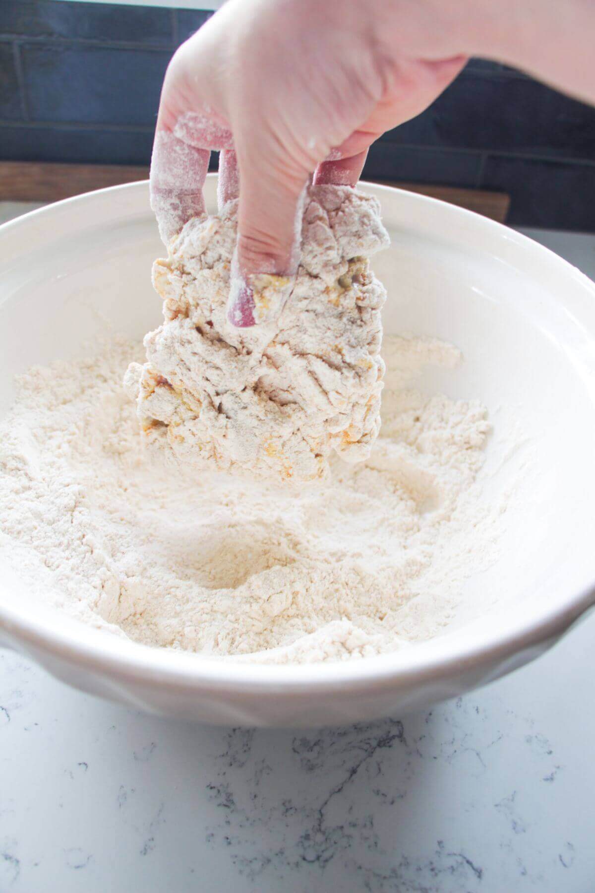 Hand dredging chicken thigh in flour and spices.