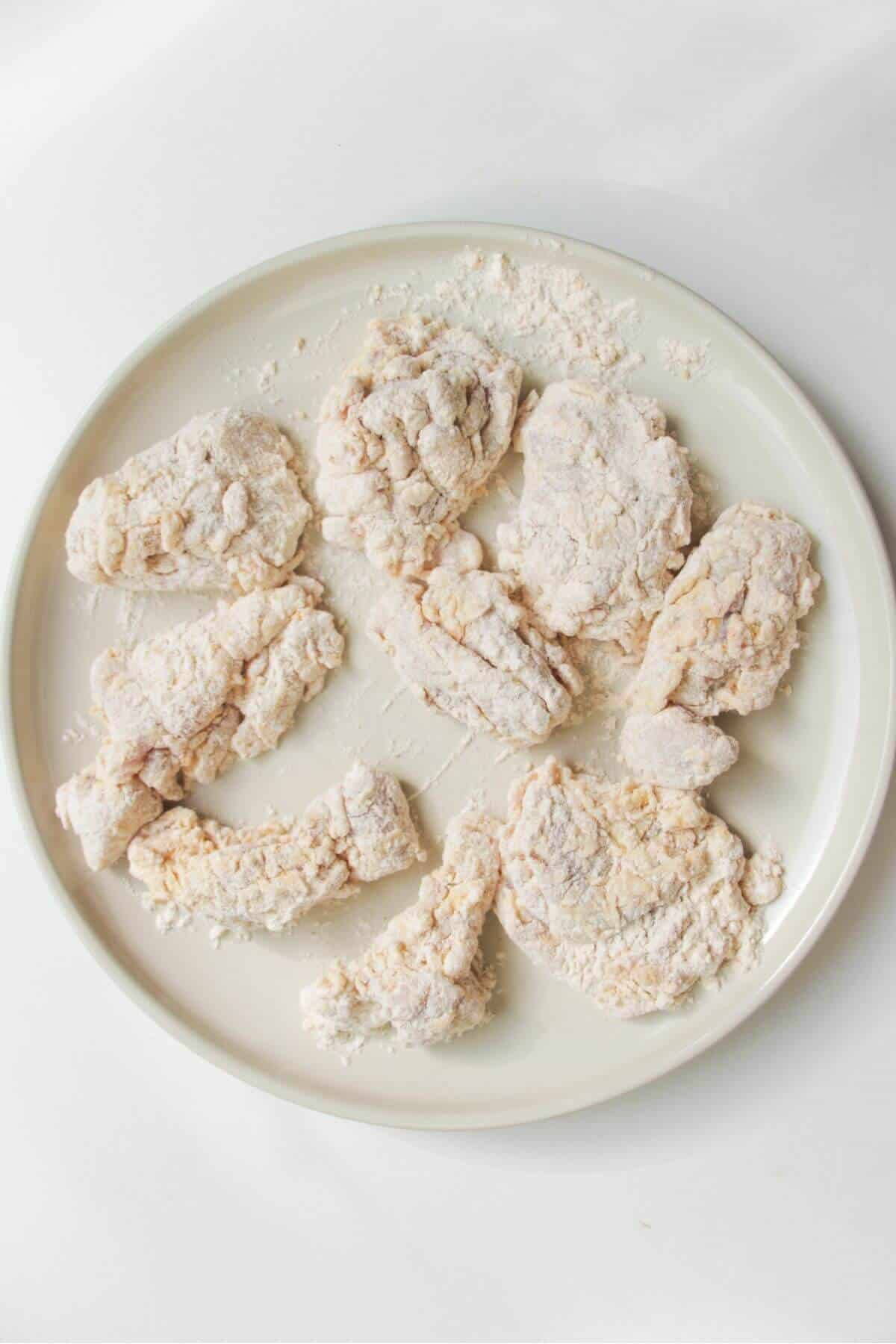 Pieces of dredged chicken on a large white plate.