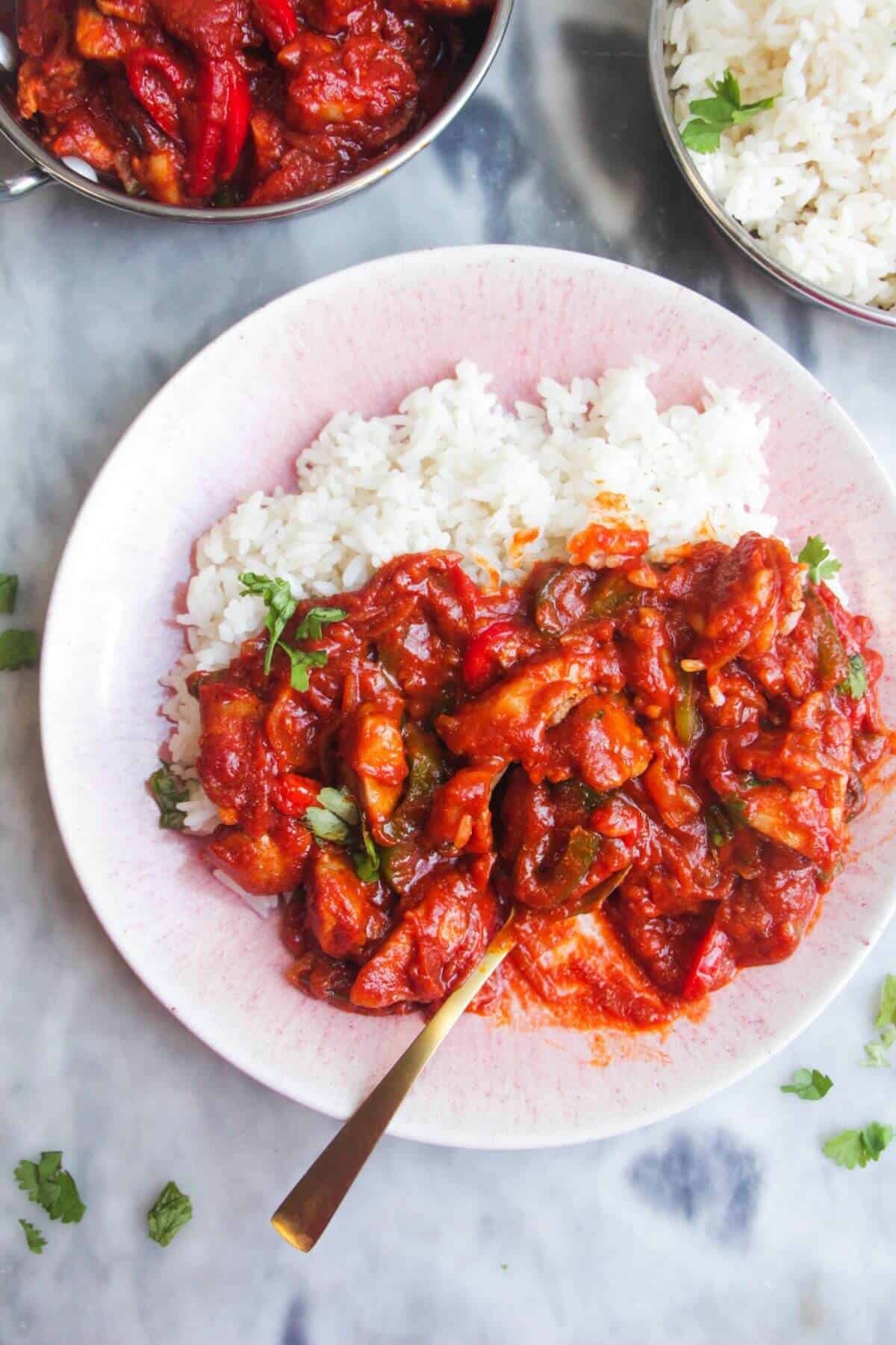 Chicken jalfrezi curry on rice on a pink plate with more curry on the side.