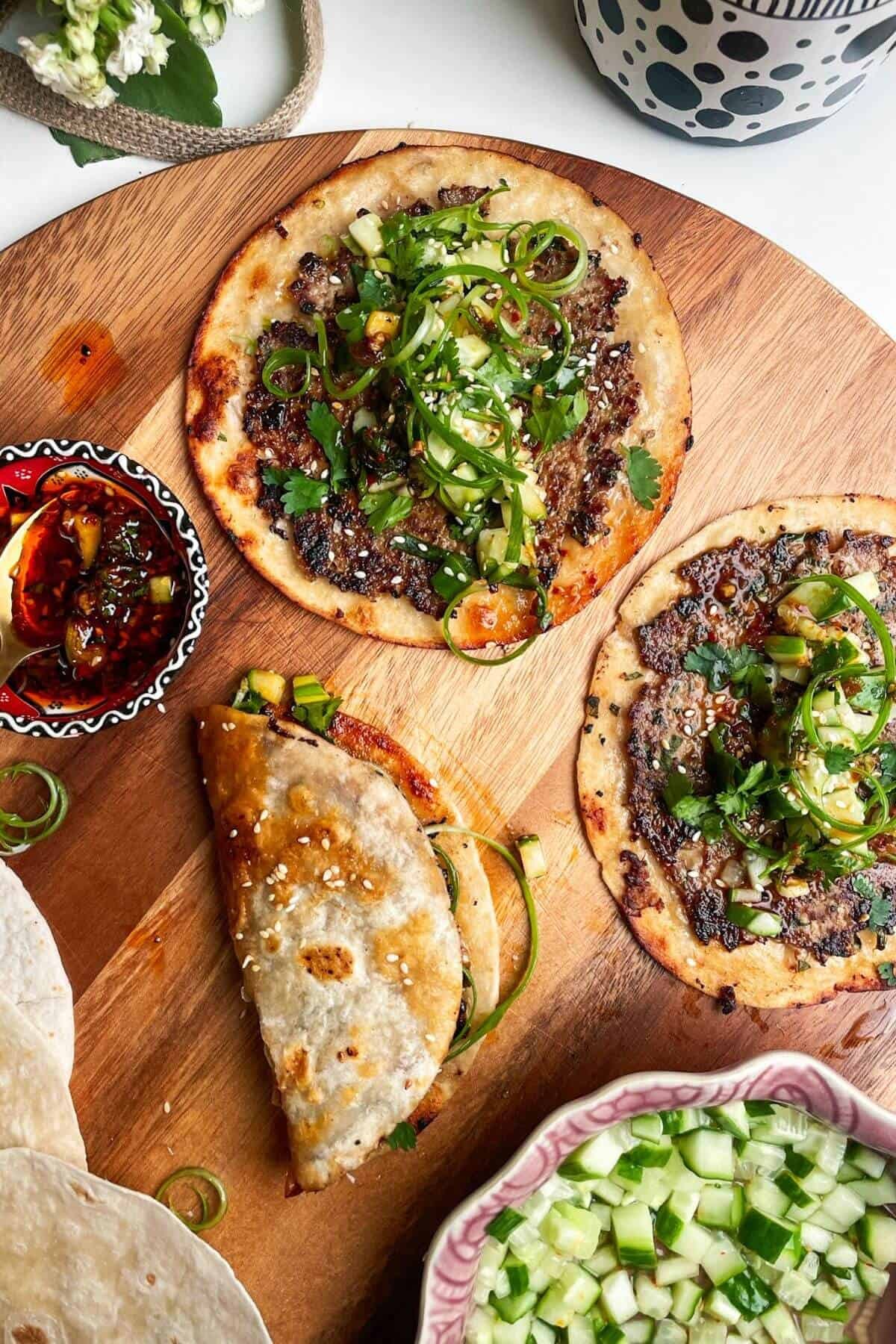 Three dumpling tacos on a wooden board with chilli oil on the side.
