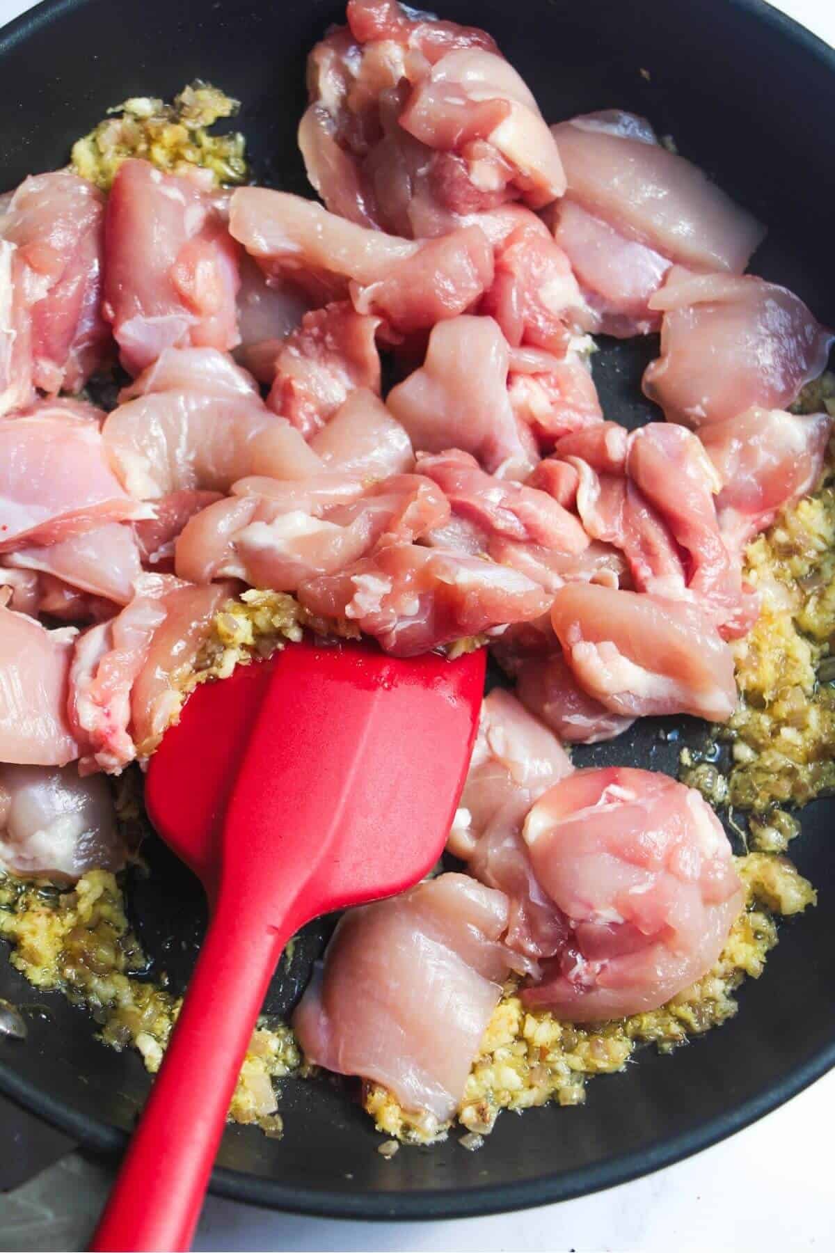 Diced chicken in a frying pan with onion and garlic.
