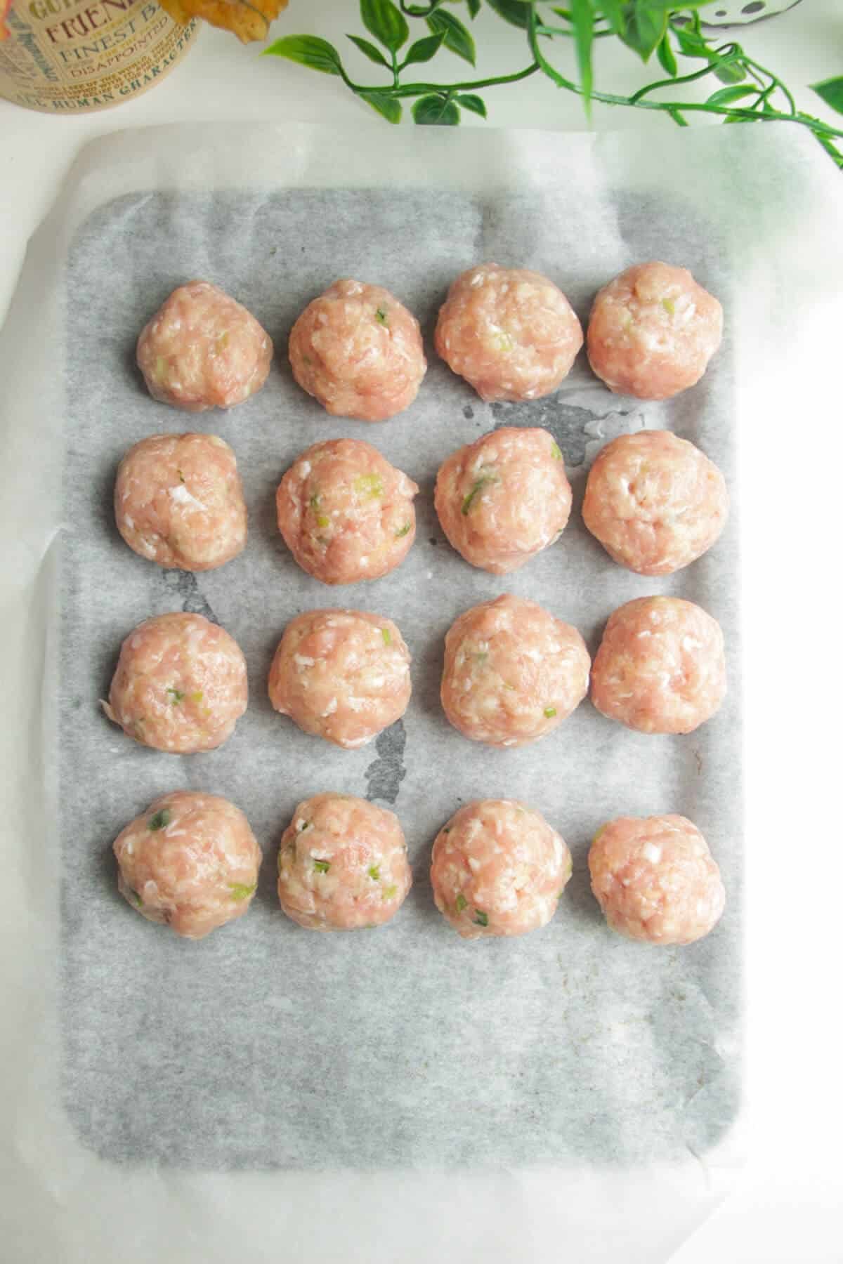 Chicken meatballs on a parchment paper lined oven tray.
