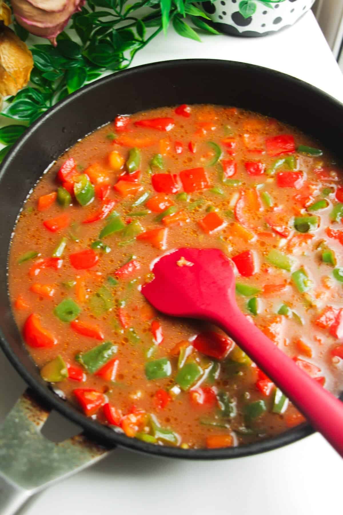 Sauce added to bell peppers in a frying pan.