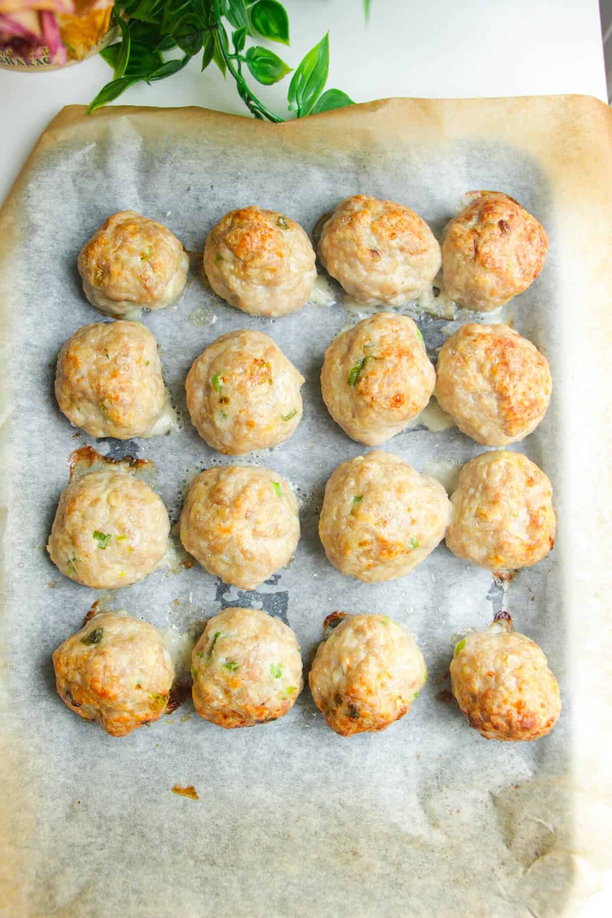Chicken meatballs baked on a lined oven tray.
