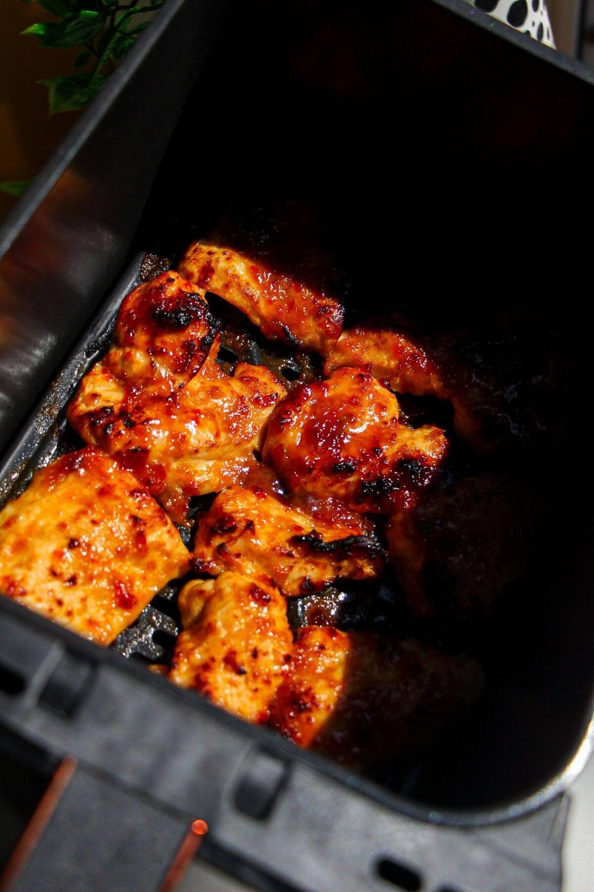 Cooked, charred chicken pieces in an air fryer basket.