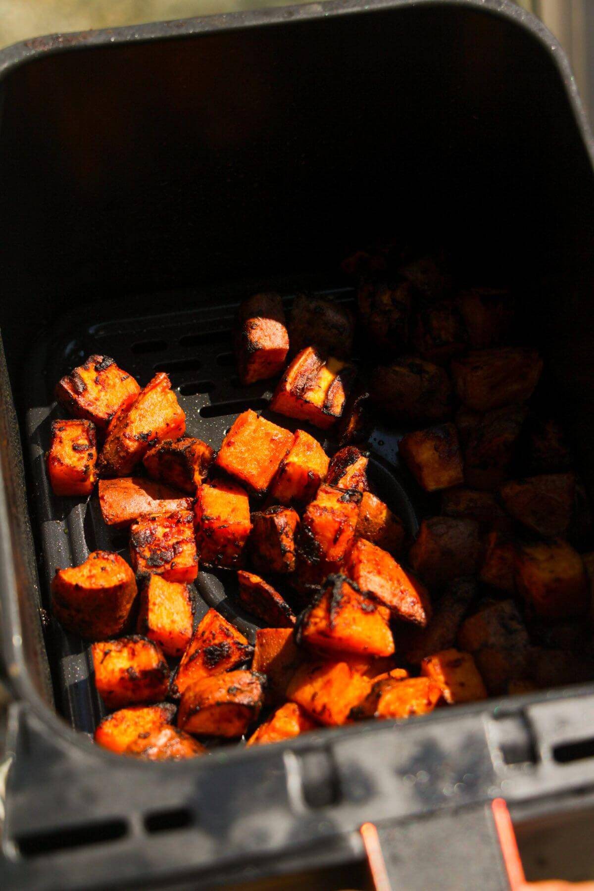 Cooked sweet potato cubes in an air fryer basket.