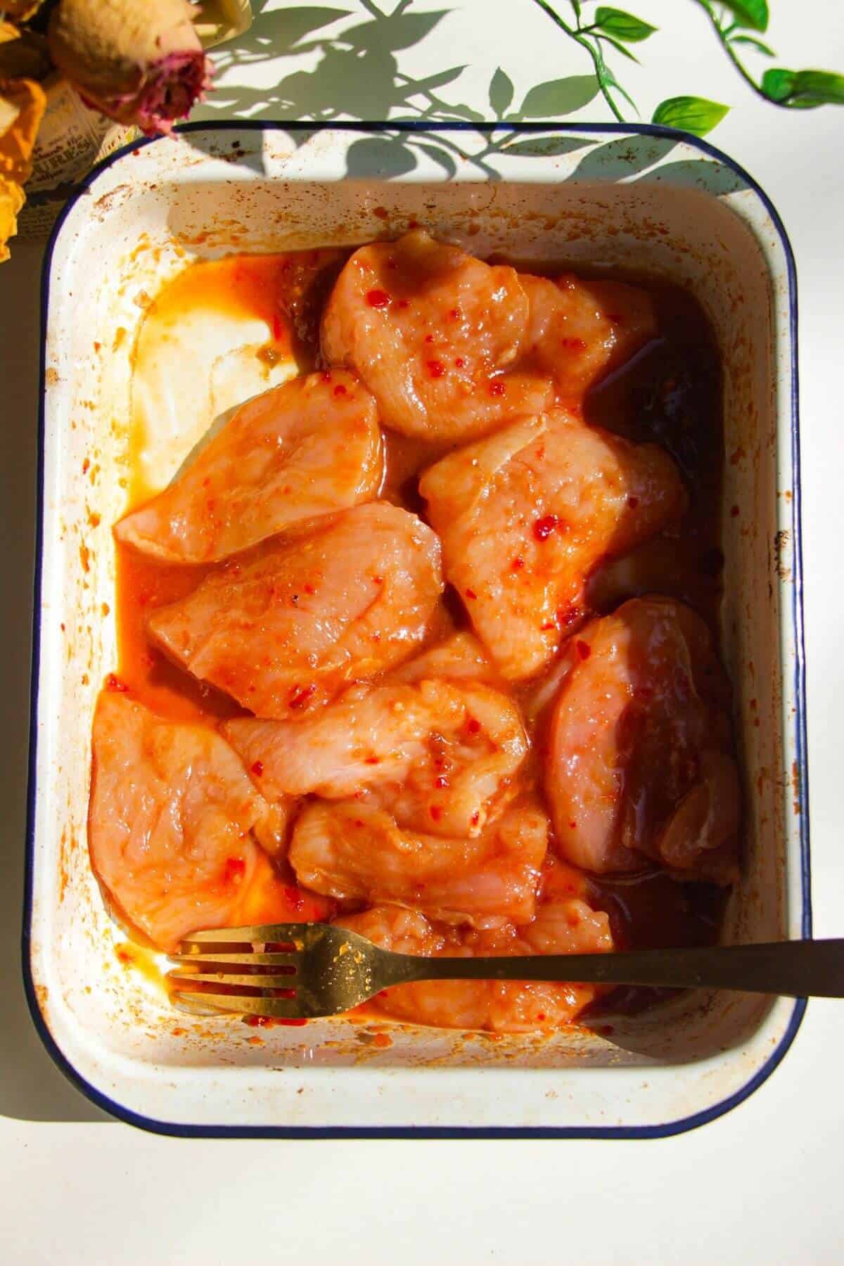 Chicken breast marinating in white dish.