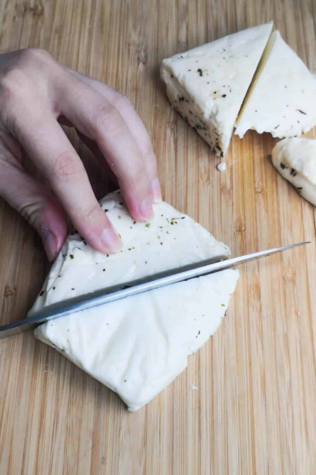 Chopping halloumi into large triangles on a wooden board.