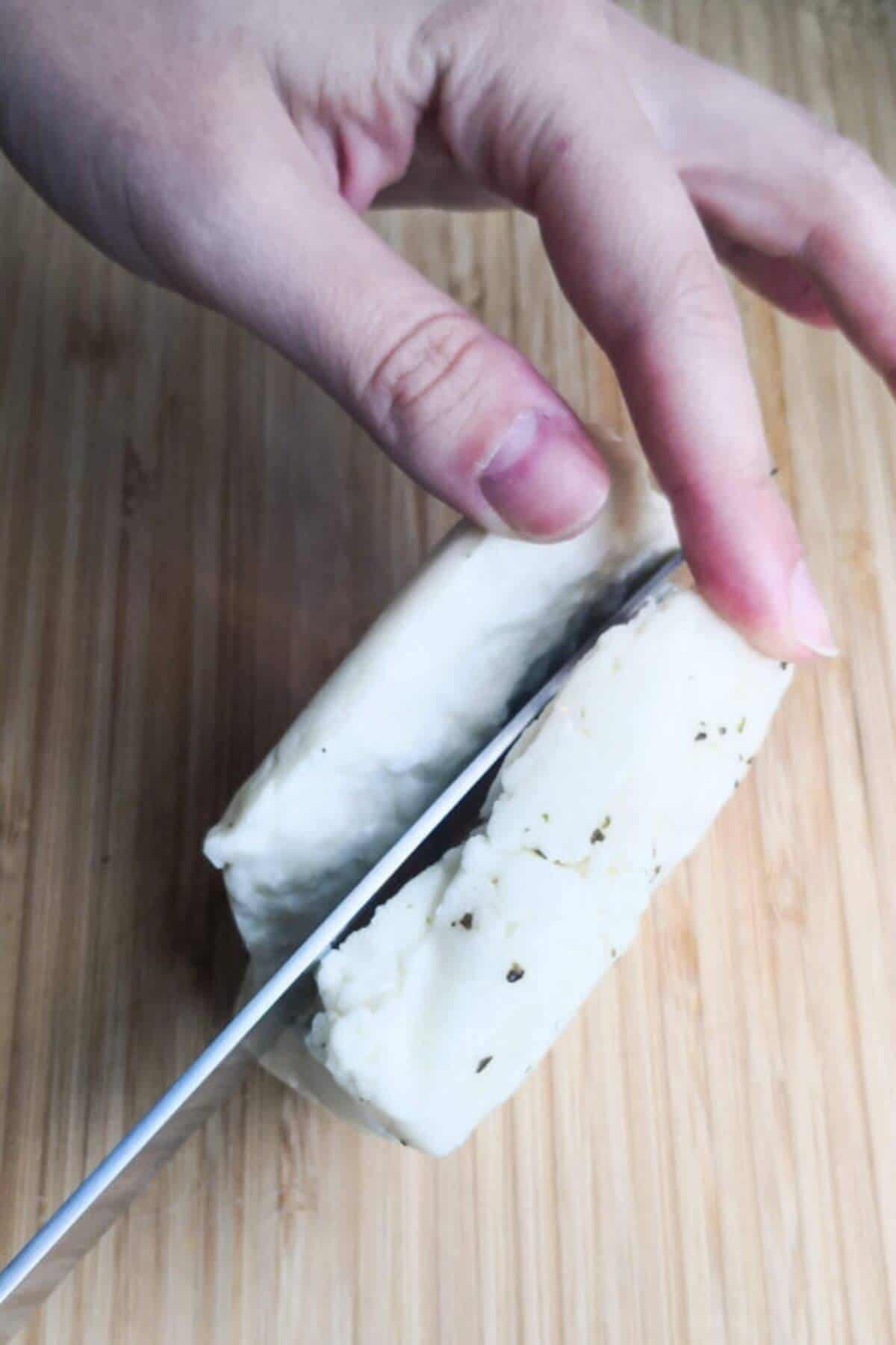 Chopping halloumi block in half on a wooden board.