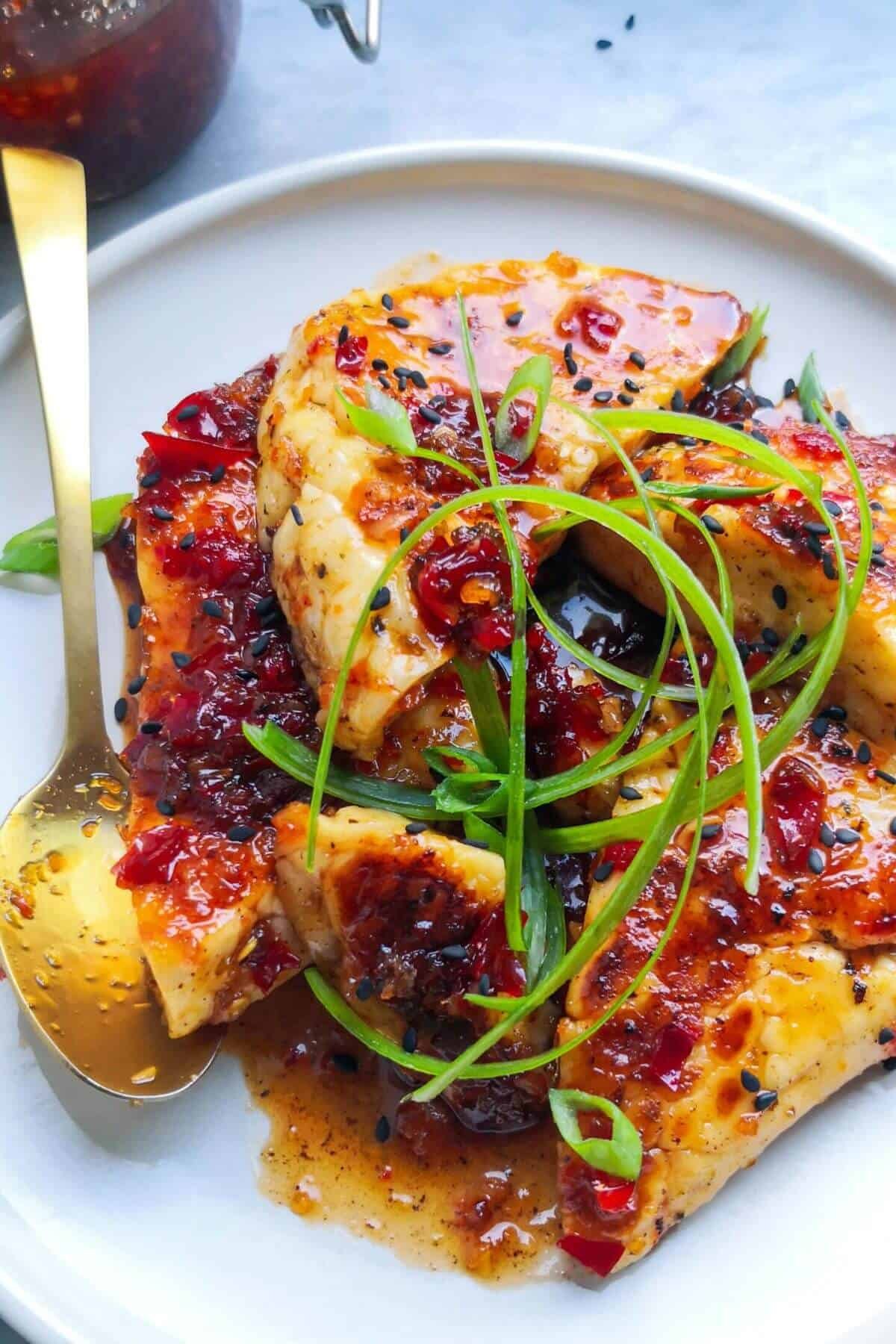 Sweet chilli glazed halloumi on a small white plate with jar of chilli jam in the background.