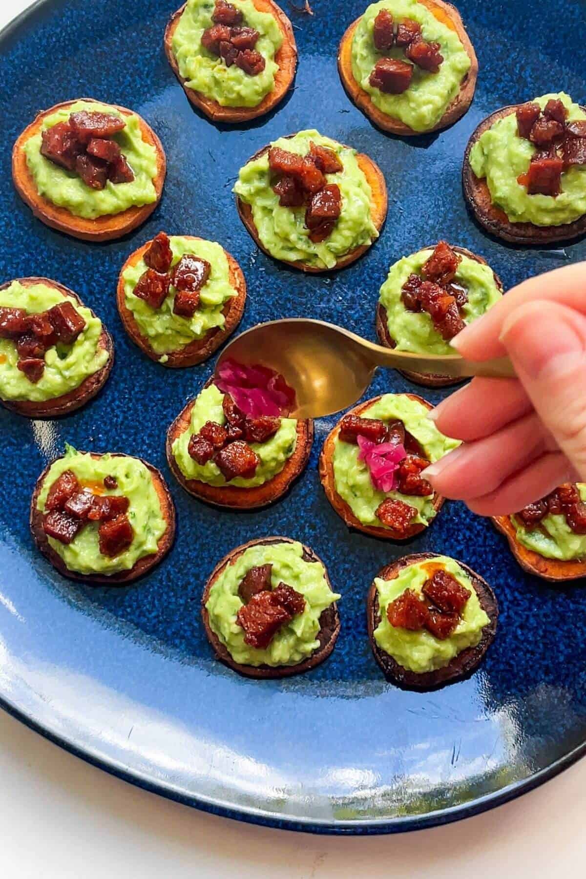 Spooning crispy chorizo onto avocado on sweet potato bites.
