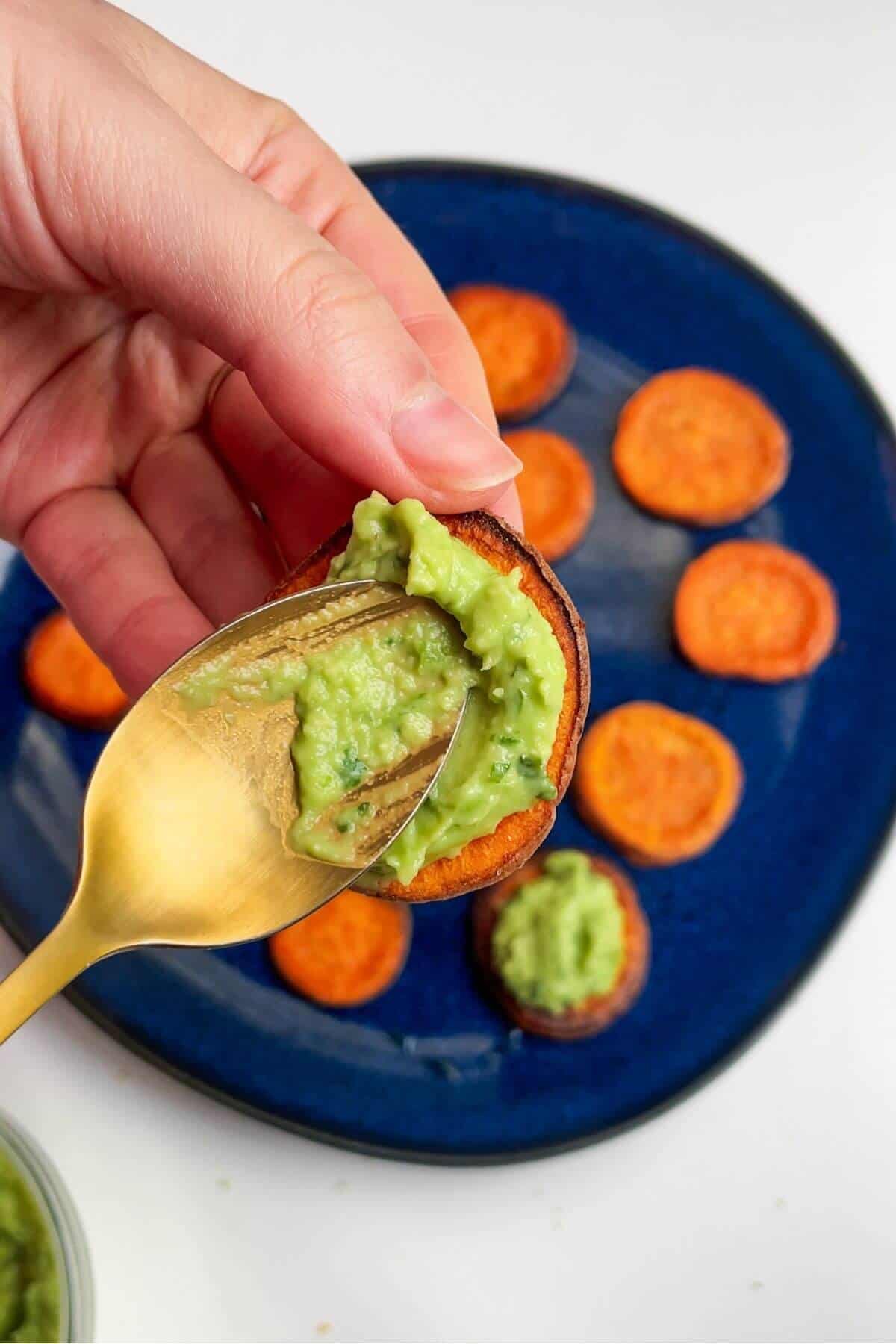 Spreading whipped avocado onto a sweet potato slice.