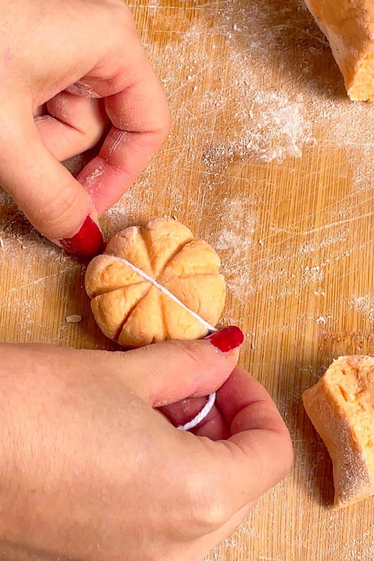 Hands holding string, pressing down on gnocchi dough to create a pumpkin shape.