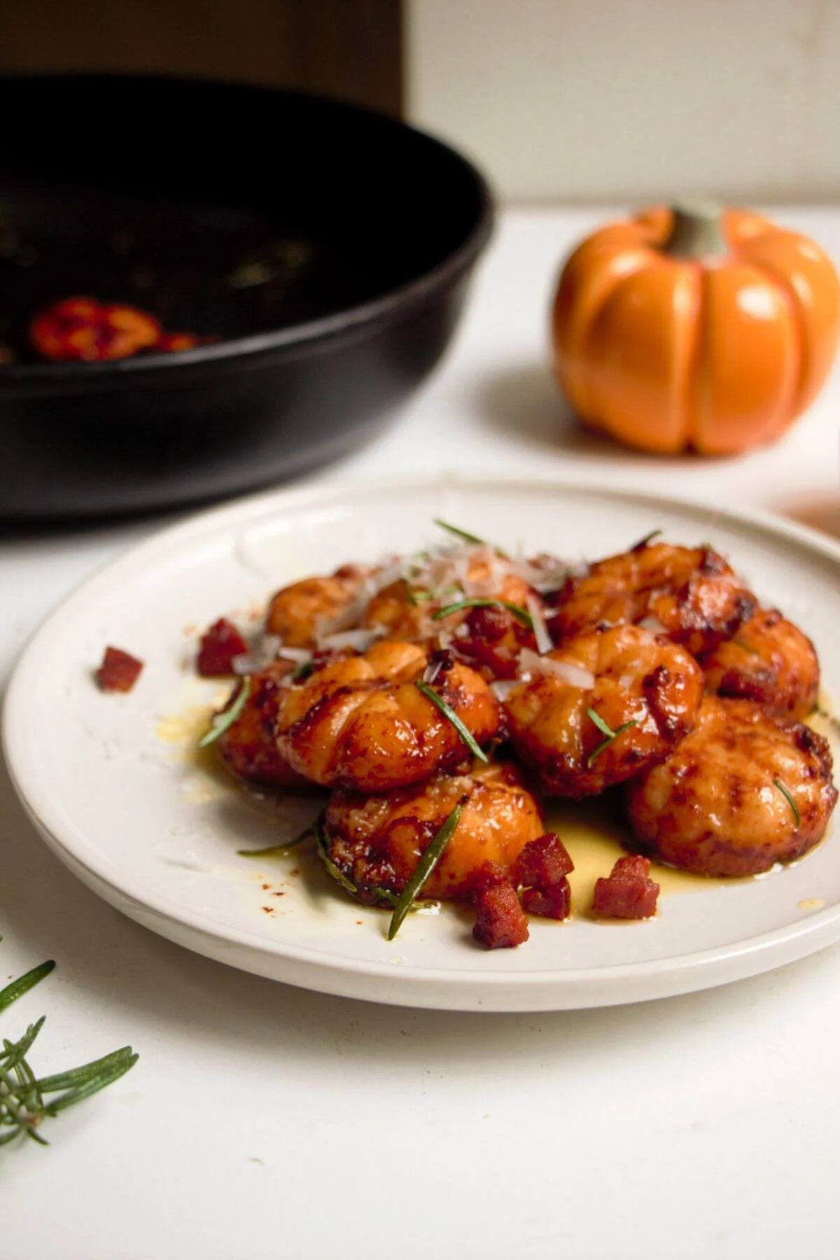 Close up of pumpkin shaped sweet potato gnocchi on a small white plate with a gold spoon.