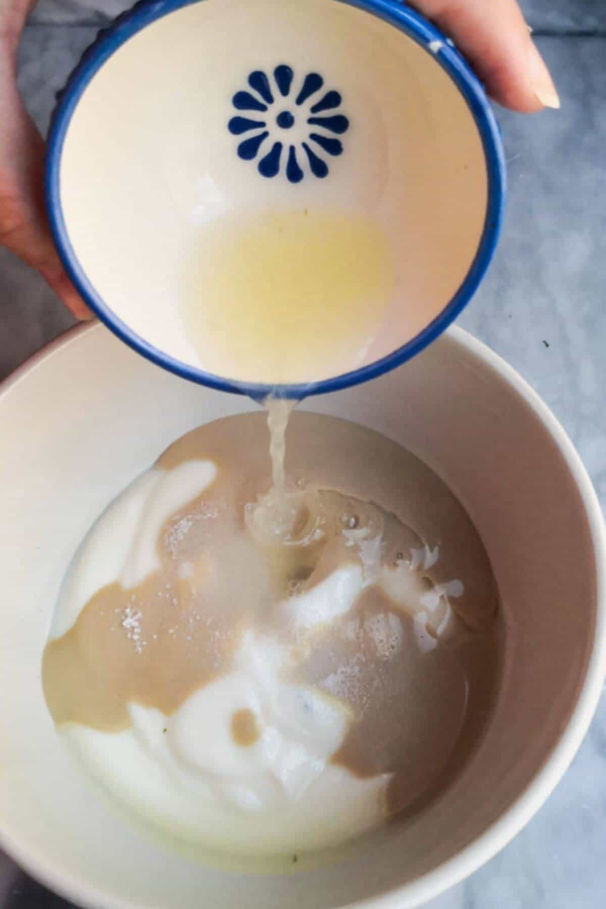 Adding lemon juice to a small white bowl with yogurt and tahini in it.