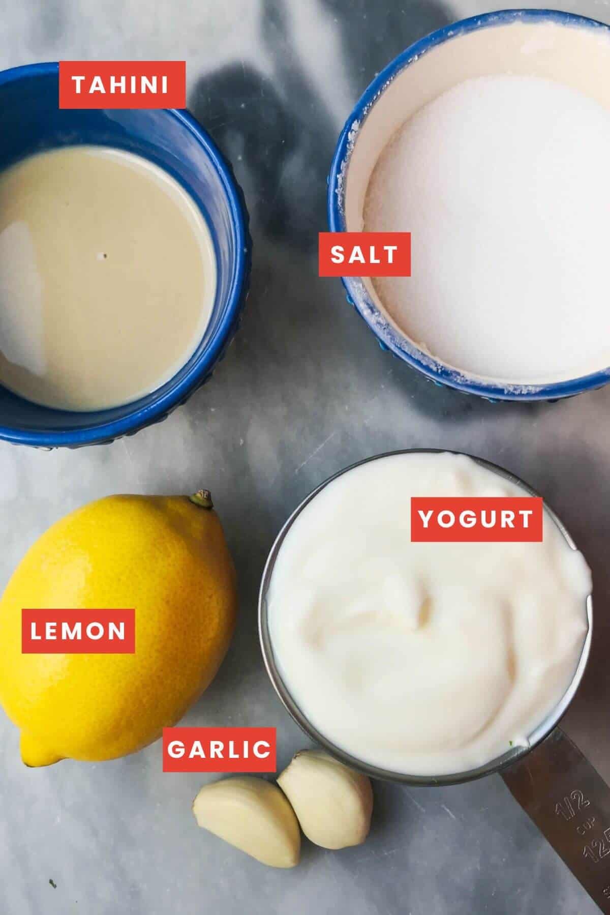 Ingredients for tahini yogurt sauce laid out on a grey marble background.