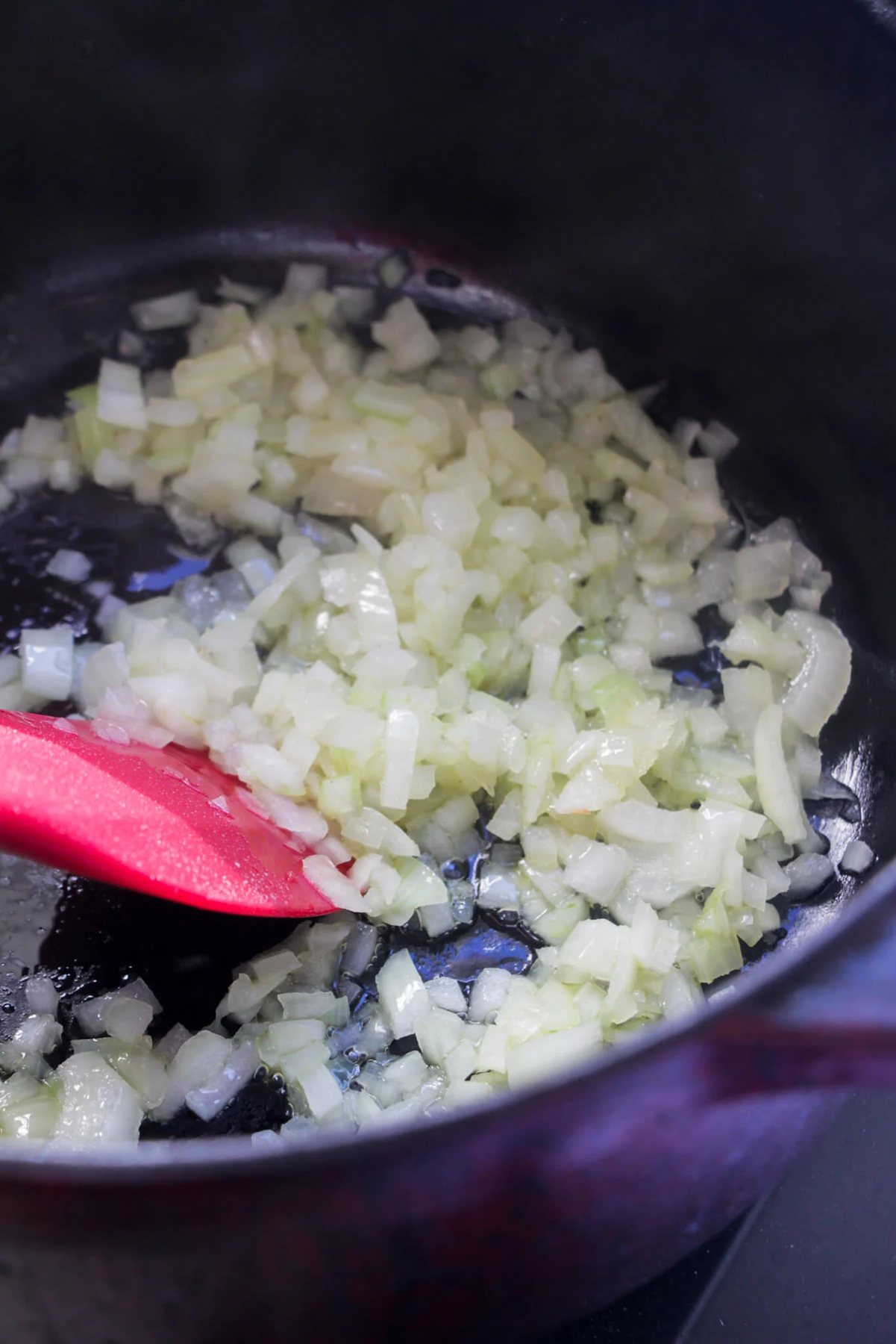 Red spatula stirring onion in a large black pot.