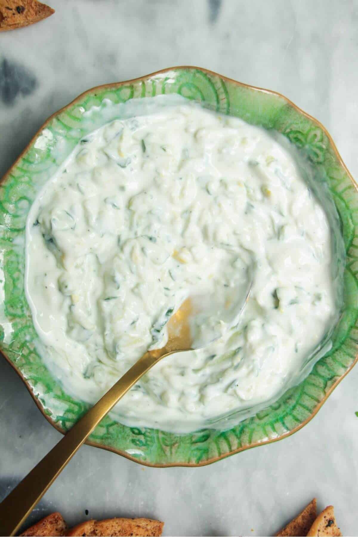 Tzatziki sauce mixed in a small green bowl on a grey marble surface.
