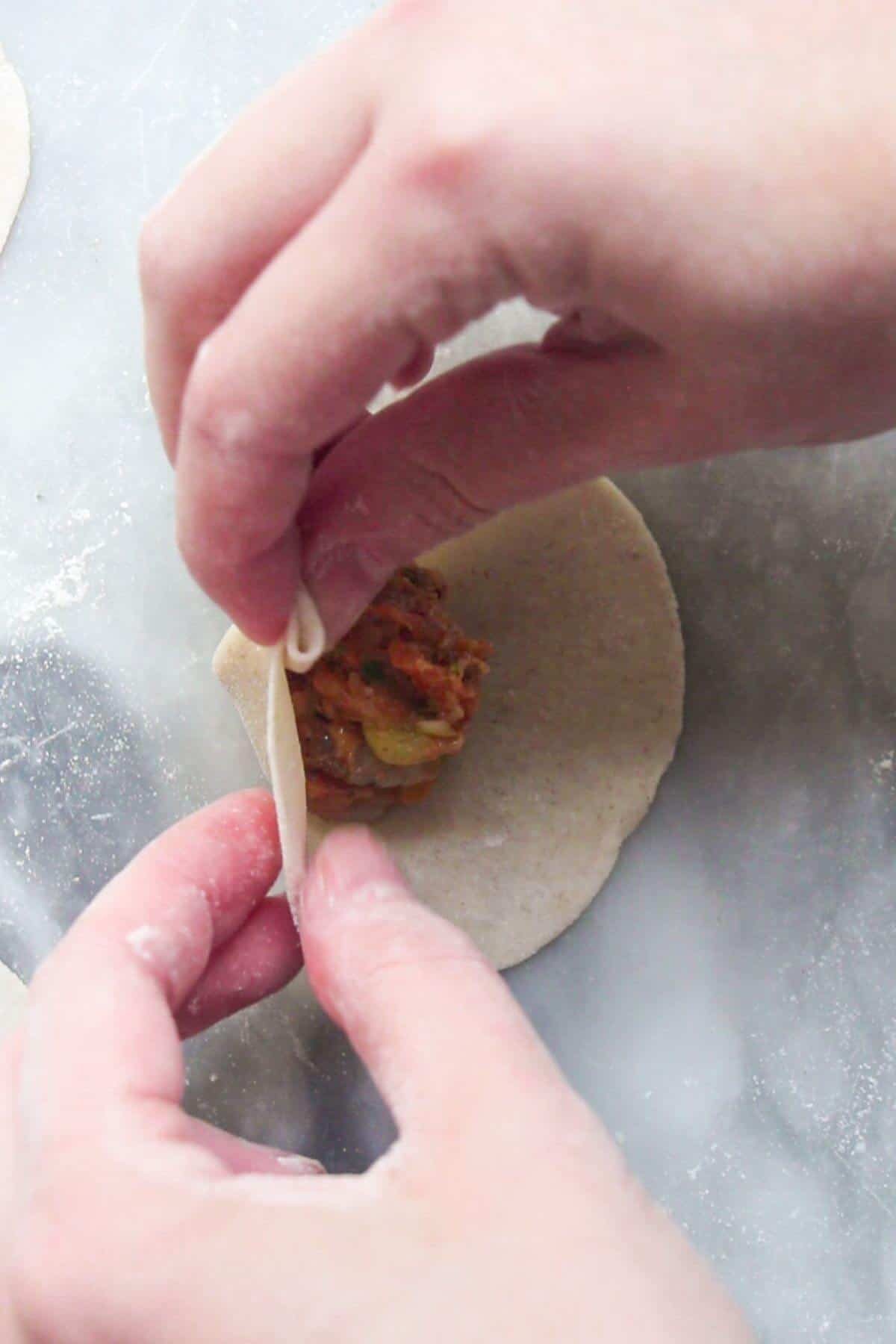 Hands folding a dumpling.