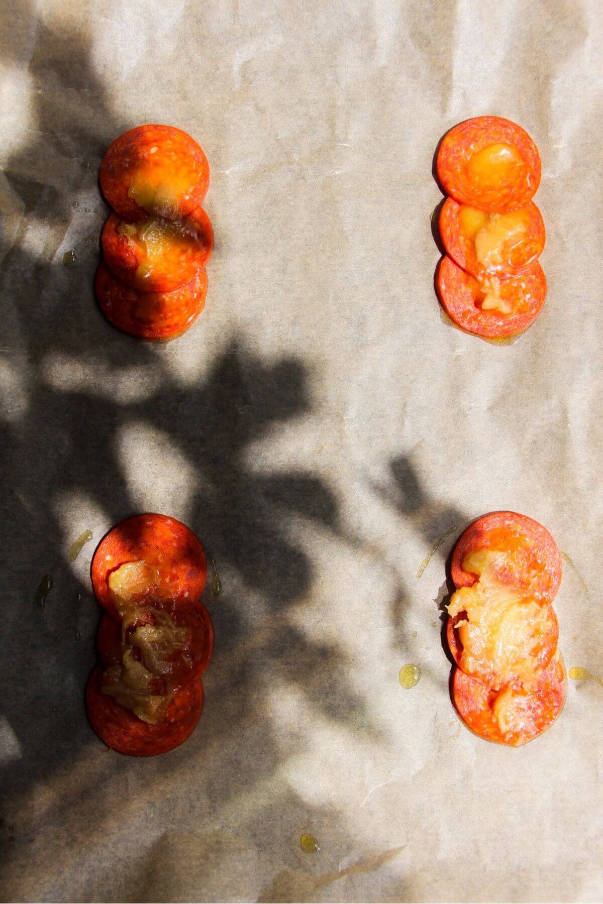Confit garlic on top of pepperoni slices on a lined baking tray.