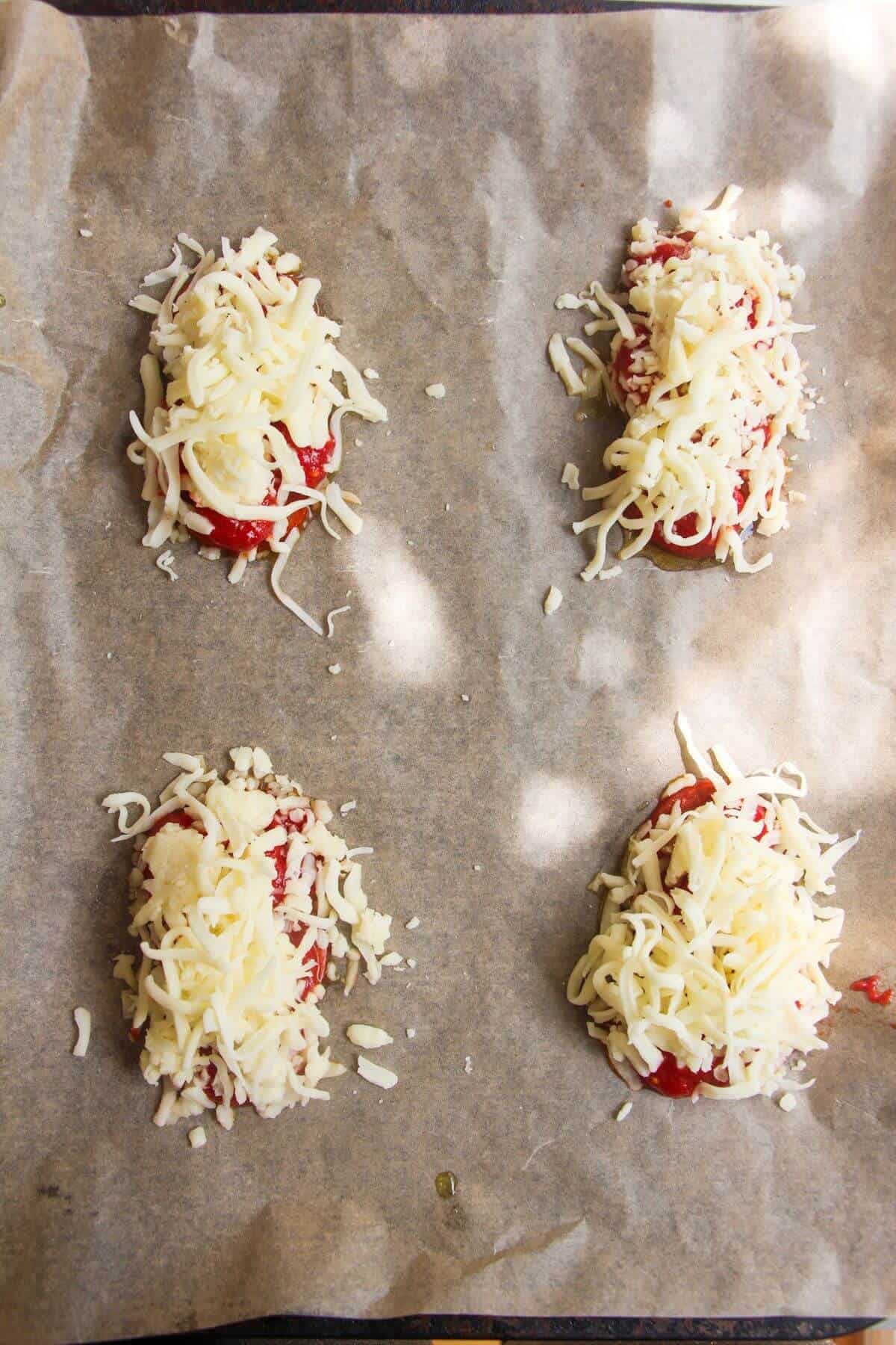 Grated mozzarella on top of pepperoni and tomatoes on a lined baking tray.