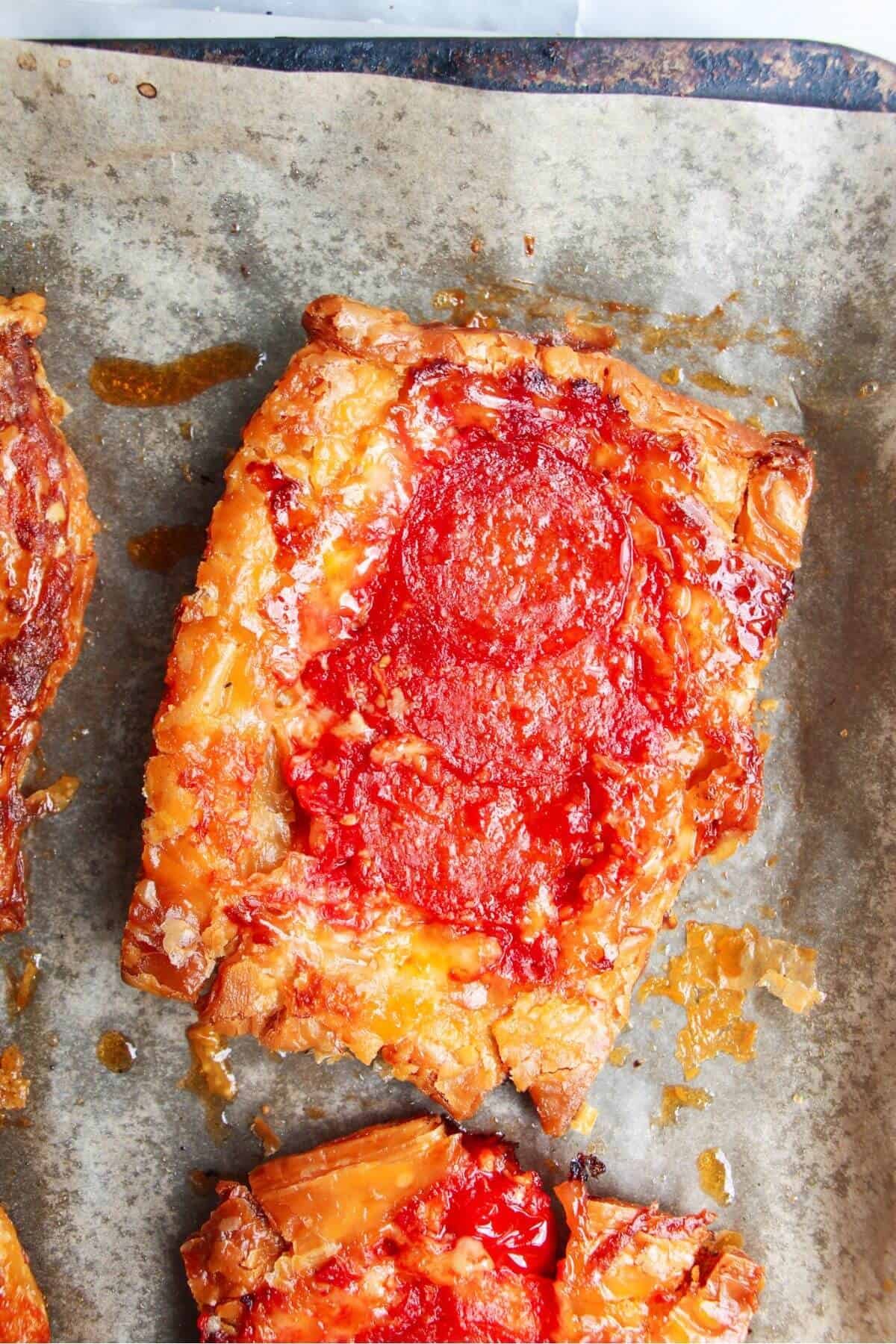 Close up of baked upside down puff pastry pizza tart on a lined baking tray.